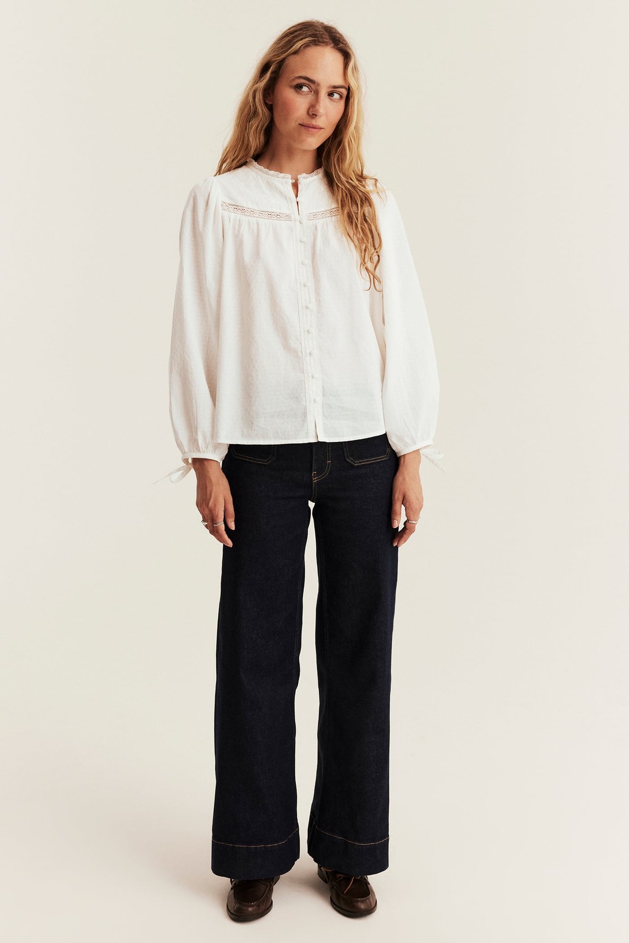 White lace blouse, dark blue wide-leg jeans, and brown loafers on female model.