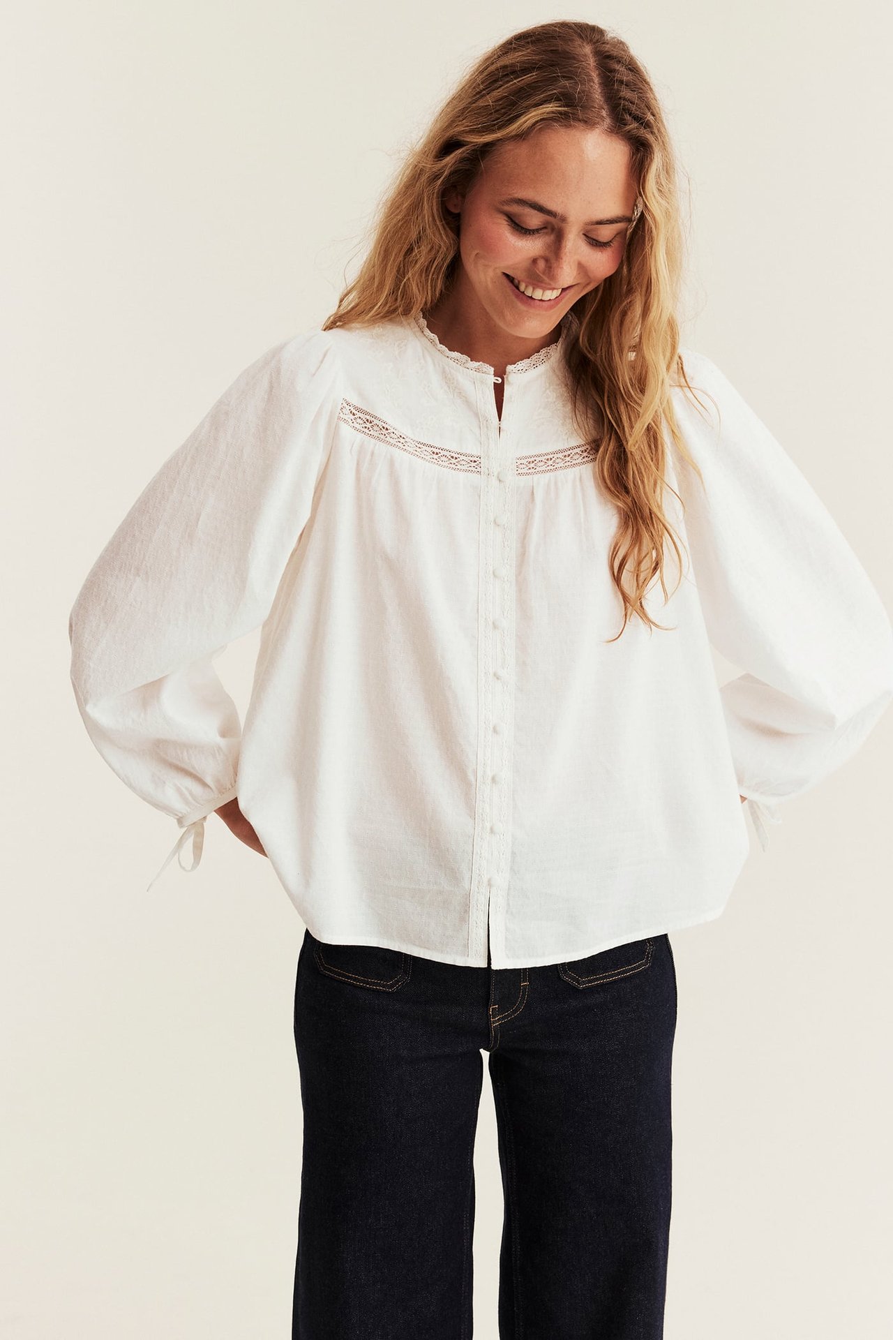 Front view, female model in a white lace blouse and dark blue wide-leg jeans.