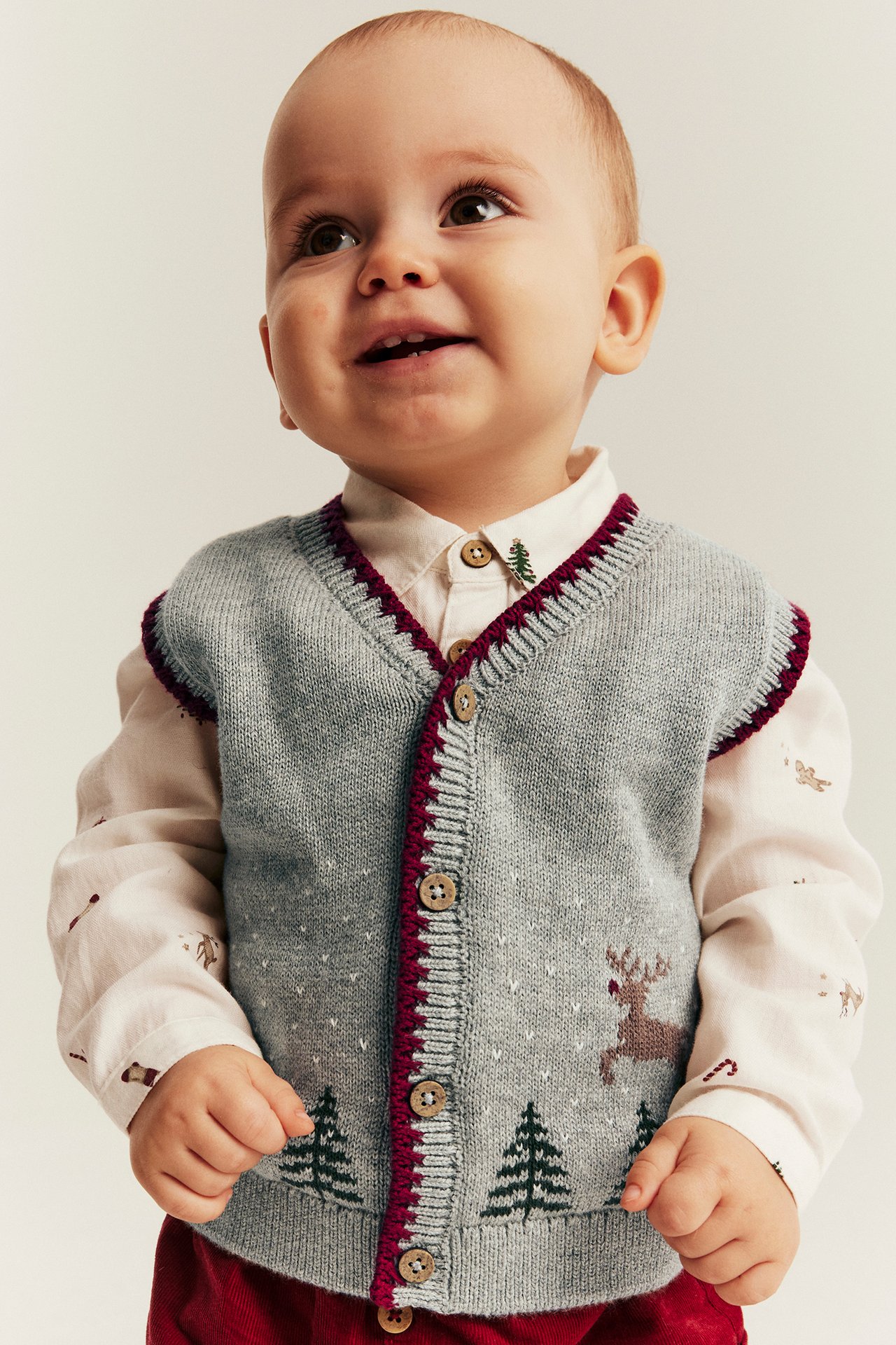 Vorderansicht: Baby trägt graue Strickweste mit Weihnachtsmotiven über einem weißen Kragenhemd.