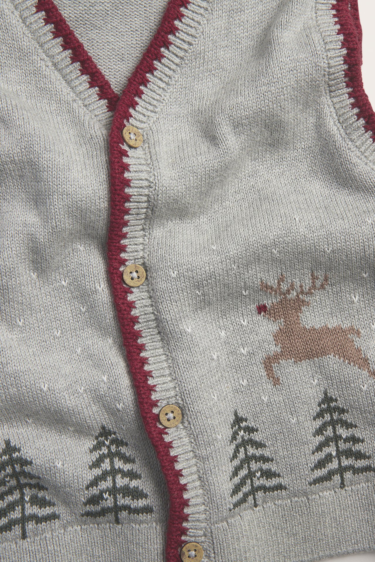 Nahaufnahme einer grauen gestrickten Kinder-Weihnachtsweste mit Rentier, Tannen und rotem Saum.