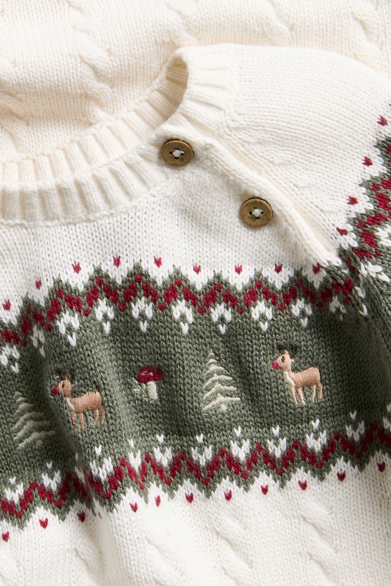 Nahaufnahme einer cremefarbenen Fair Isle Strickjacke für Babys mit Waldstickerei, zwei Holzknöpfen.