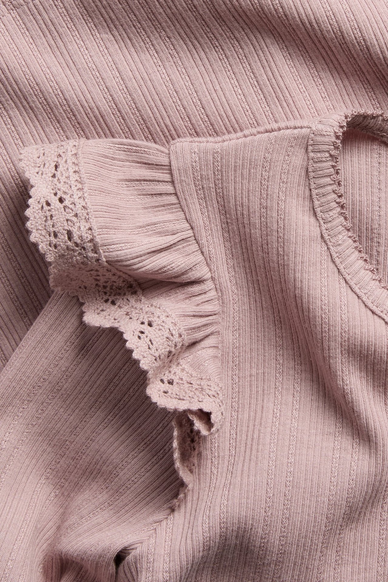 Close-up of a pink ribbed knit top with ruffled sleeves and lace trim.