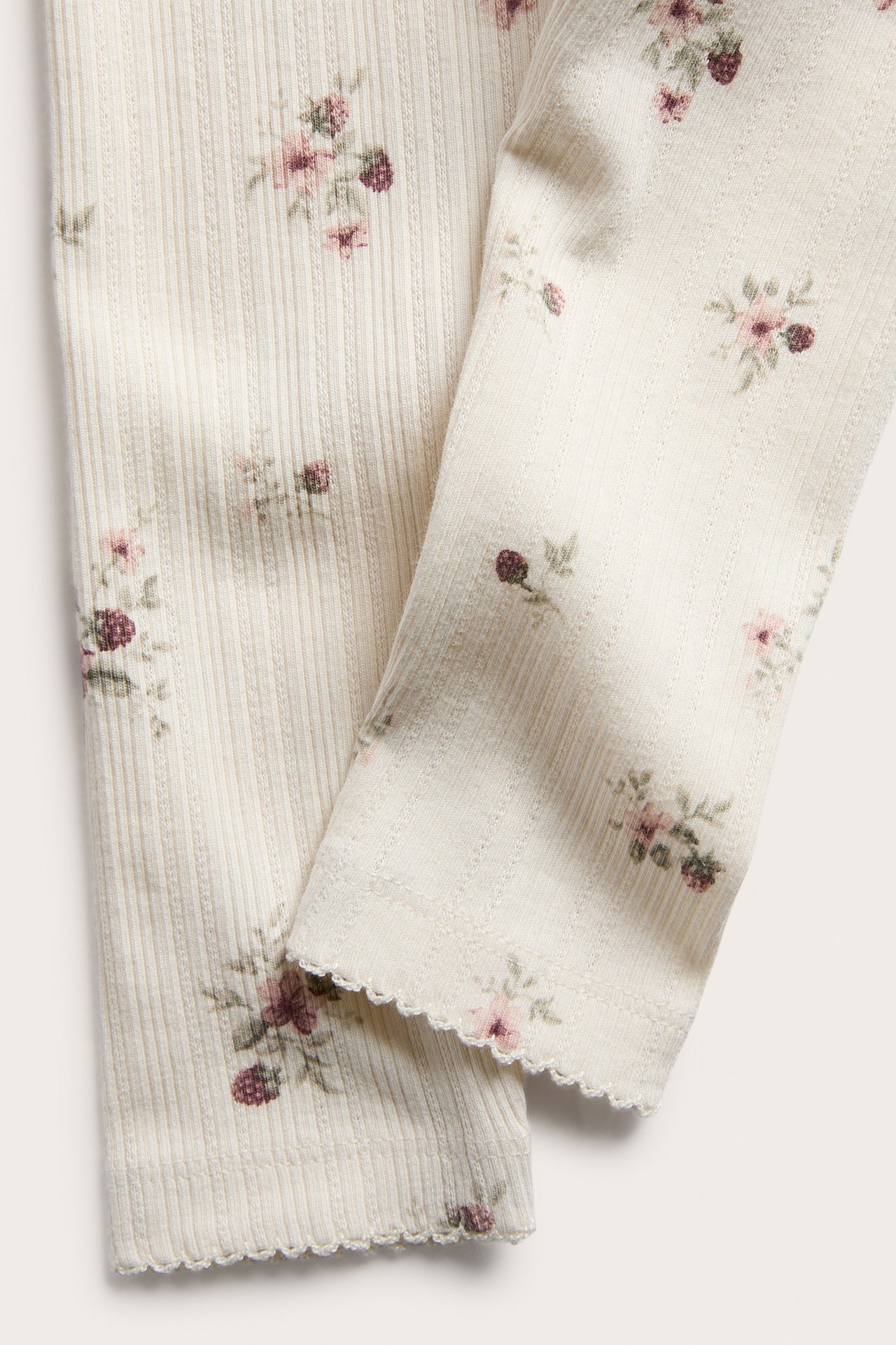 Close-up of cream ribbed knit garment with pink floral and purple berry print, featuring scalloped edges.