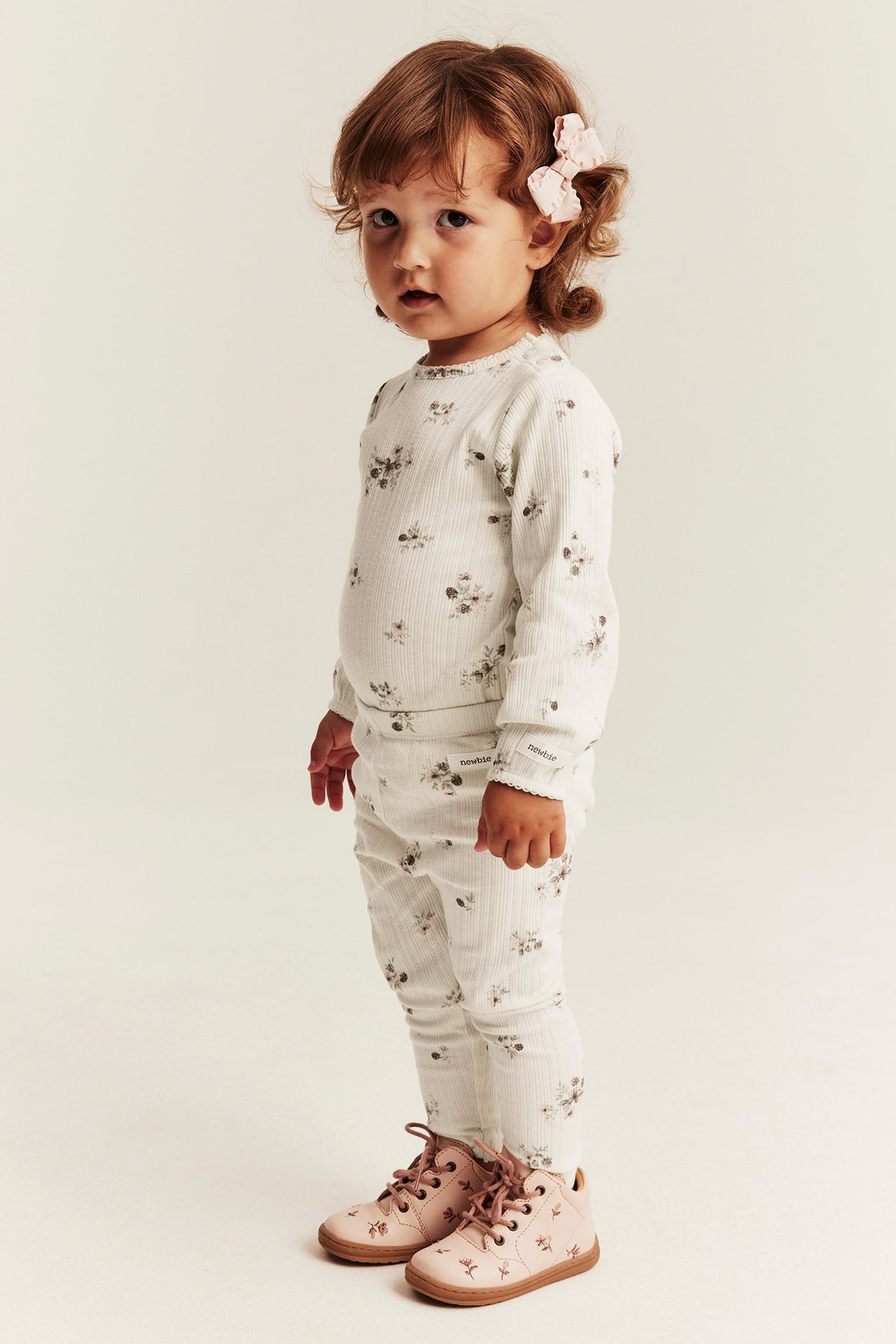 Side view of baby girl in a ribbed floral long-sleeved top, matching leggings, and pink floral boots.