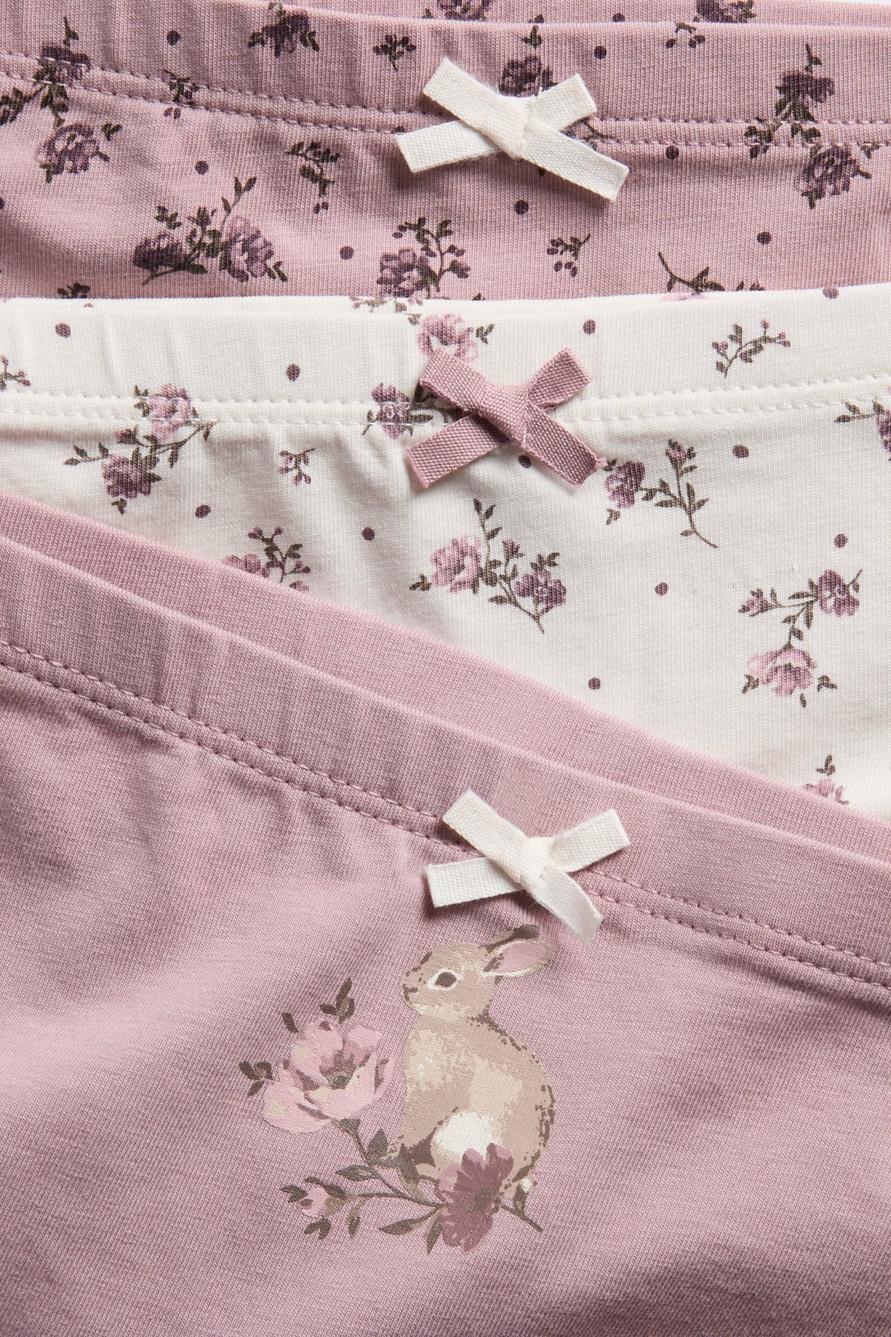 Nahaufnahme von Kinder-3er-Pack rosa und weißen Boxershorts mit Blumen- und Kaninchenprints, verziert mit Schleifen.