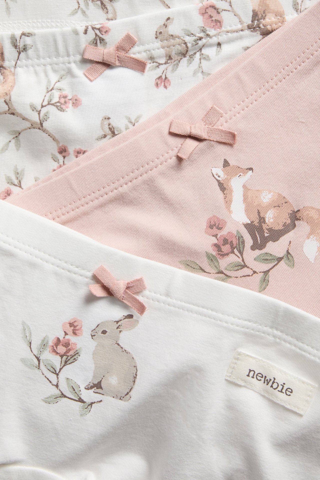 Nahaufnahme von Kinder-3er-Pack Boxershorts in Offwhite und Hellrosa mit Tiermotiven und kleinen Schleifen.