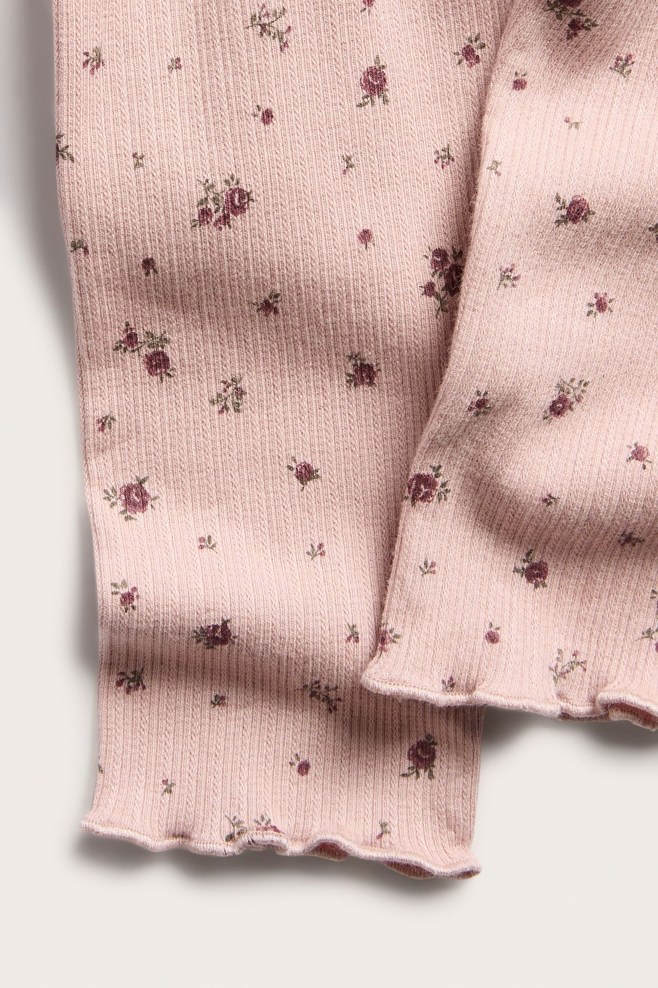 Nahaufnahme von hellrosa Rippstoff mit Blumenmuster und Rüschensaum.