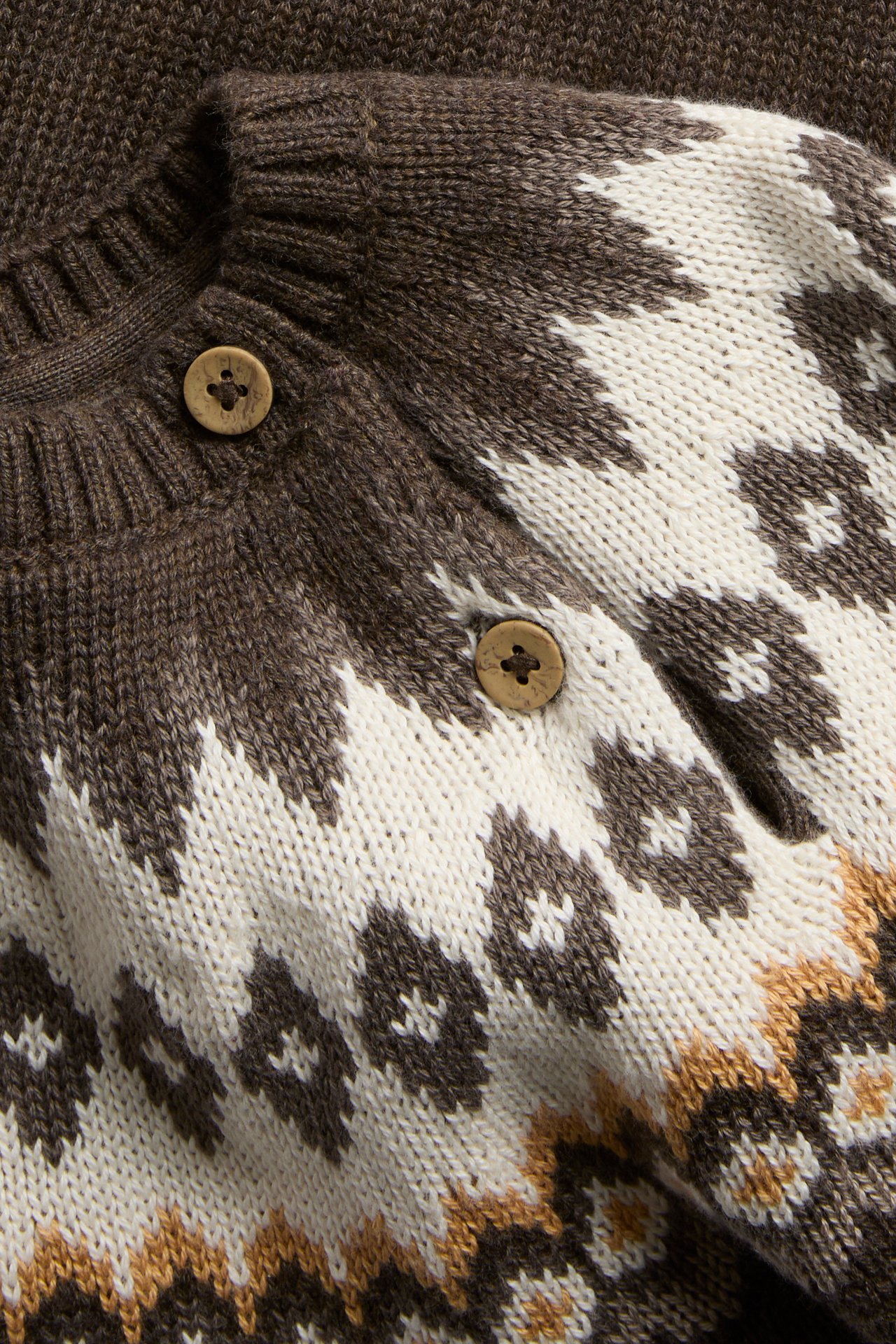 Nahaufnahme einer braun-weiß gemusterten Strickjacke mit Holzknöpfen.