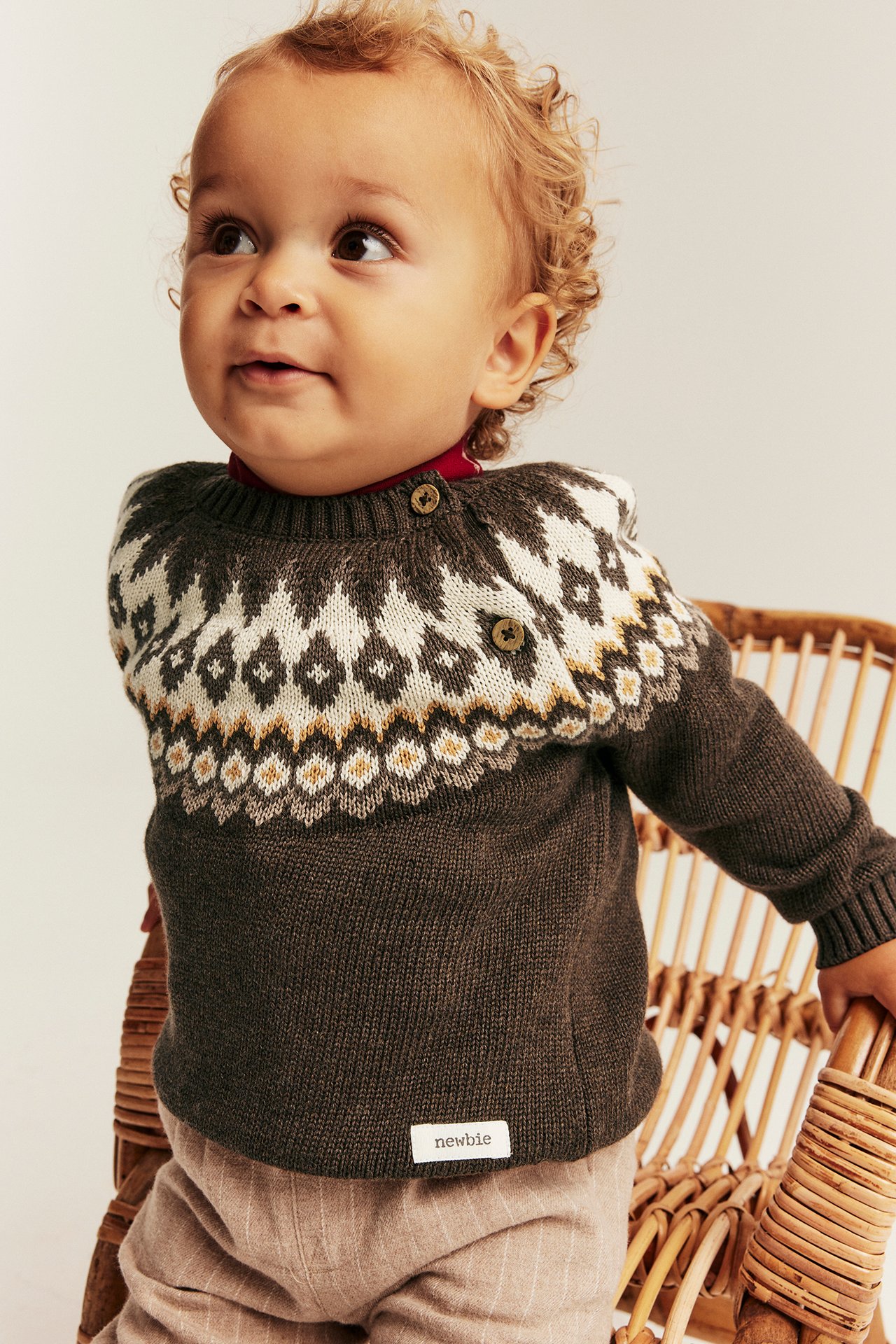 Front view of baby wearing a dark brown Fair Isle patterned sweater with light brown striped pants.