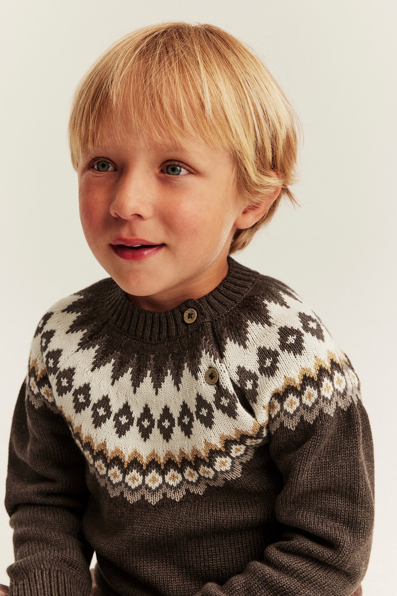Close-up front view of a kid's brown and white patterned fair isle sweater with shoulder buttons.