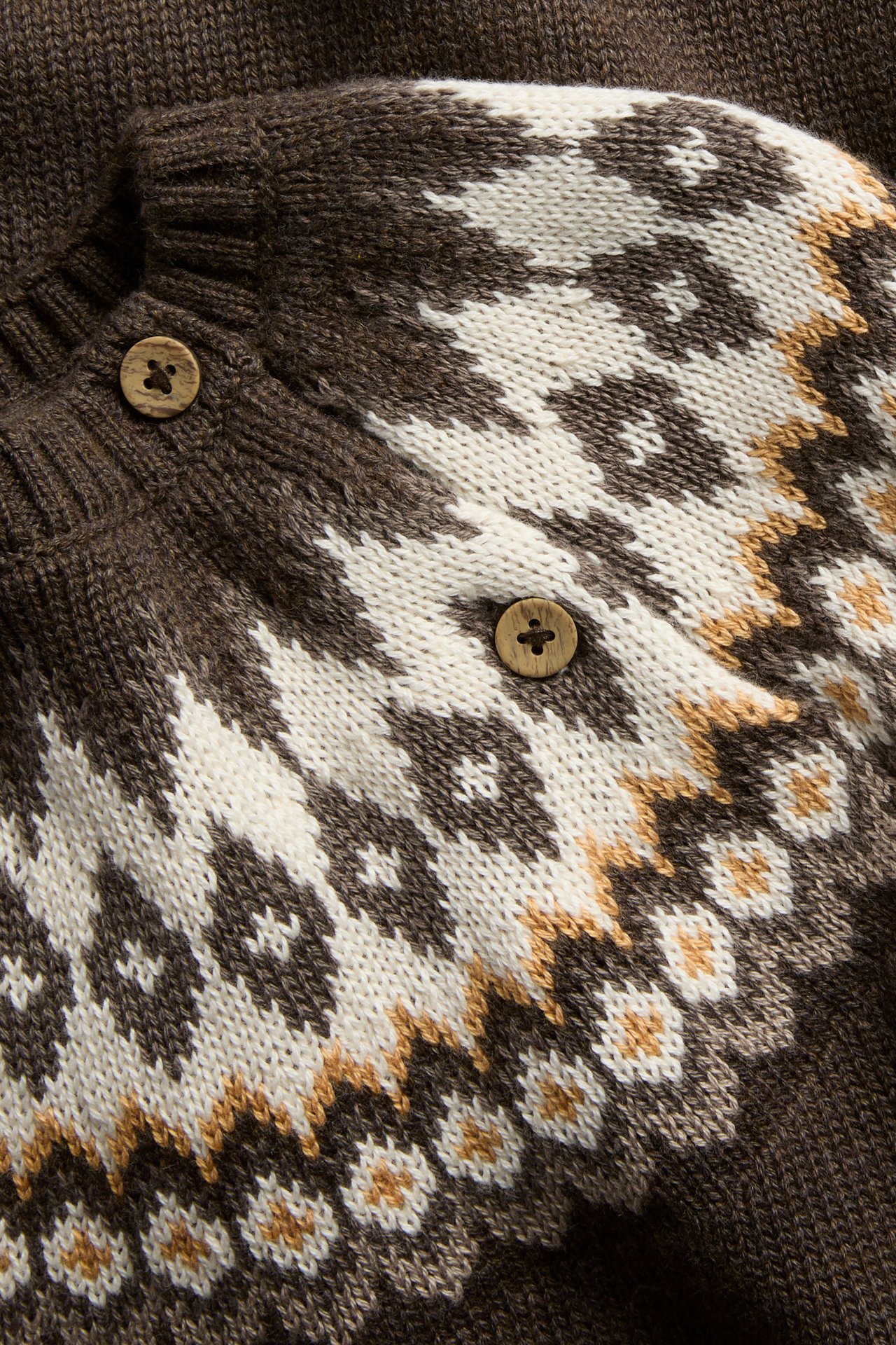 Close-up of a brown knit garment with white and tan Fair Isle pattern and wooden buttons.