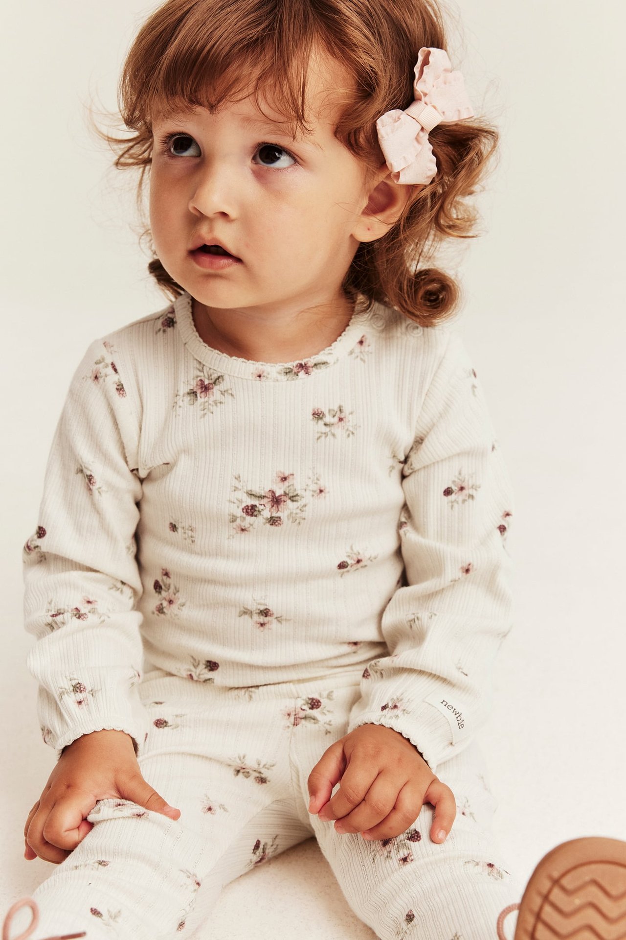 Vorderansicht eines Babys in einem cremefarbenen gerippten Langarm-Oberteil und passender Hose mit Blumenmuster.