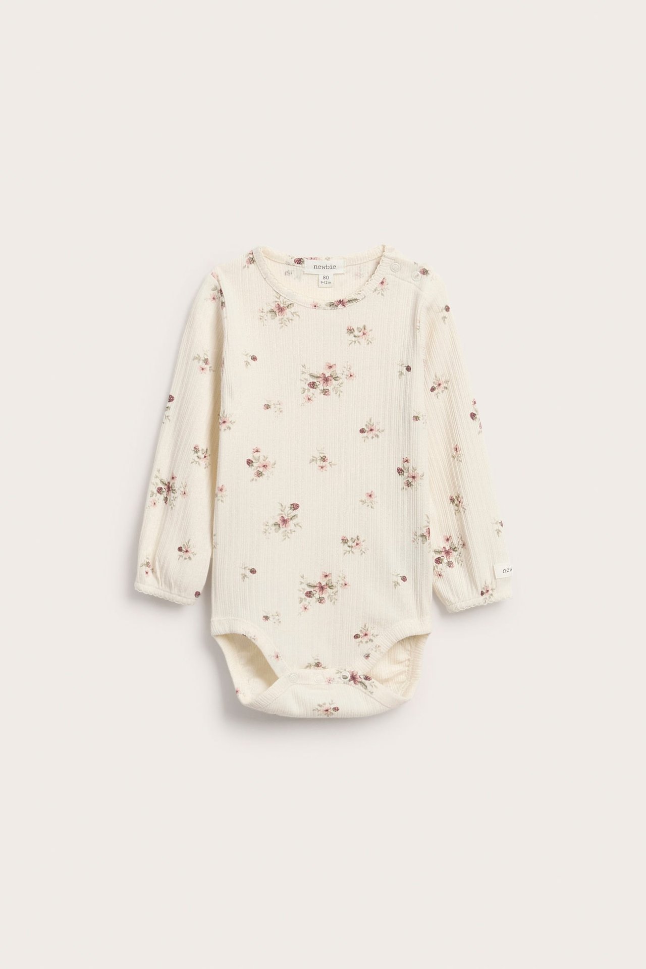 Vorderansicht eines gerippten Baby-Bodys in Creme mit langen Ärmeln und rosa Blumenmuster.