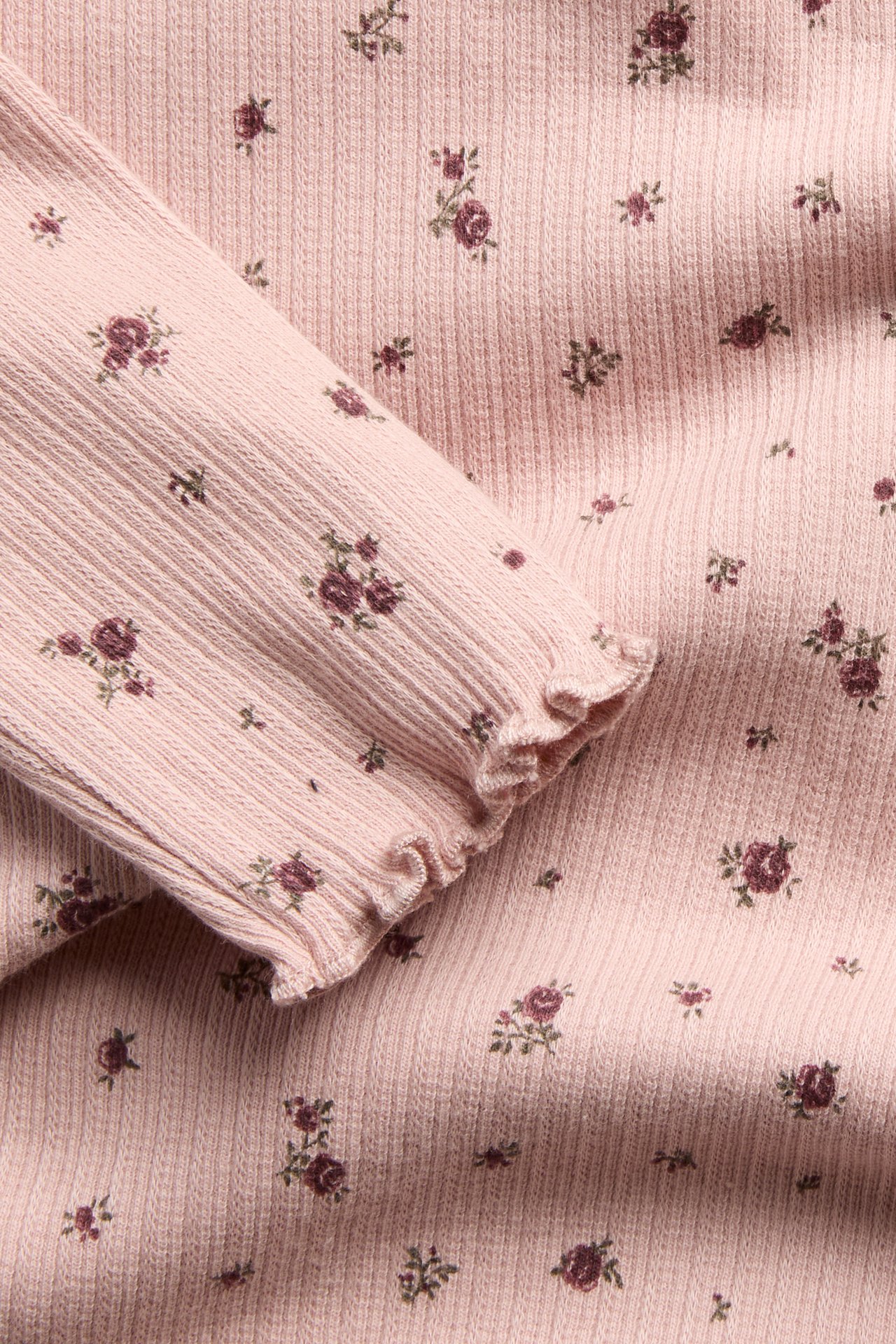 Nahaufnahme eines rosa gerippten Oberteils mit kleinem Blumenmuster und Rüschenmanschette.