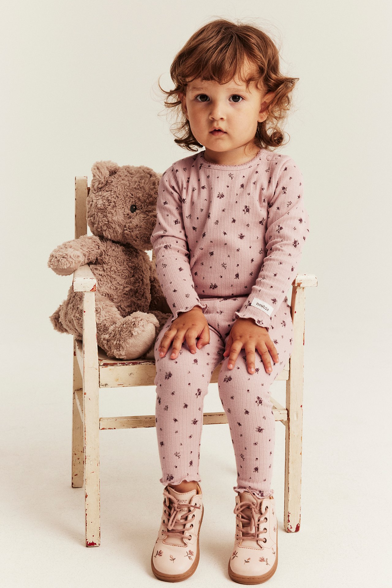 Frontansicht: Kind in rosa geripptem Oberteil, Leggings mit Blumenmuster und rosa Schnürstiefeln.