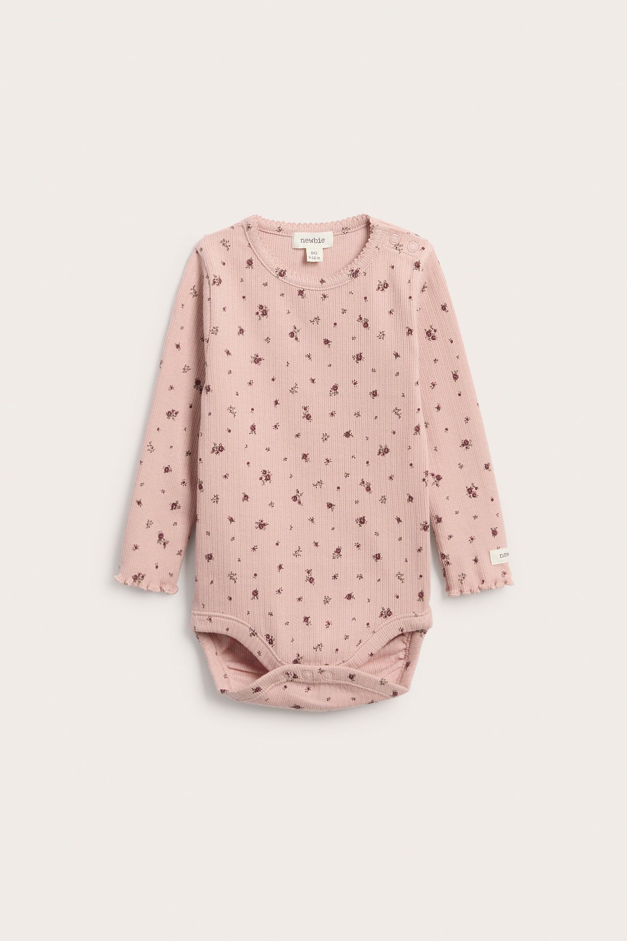 Vorderansicht eines pinkfarbenen gerippten Baby-Langarmbodys mit Blumenmuster, Rüschenbündchen und Druckknöpfen.