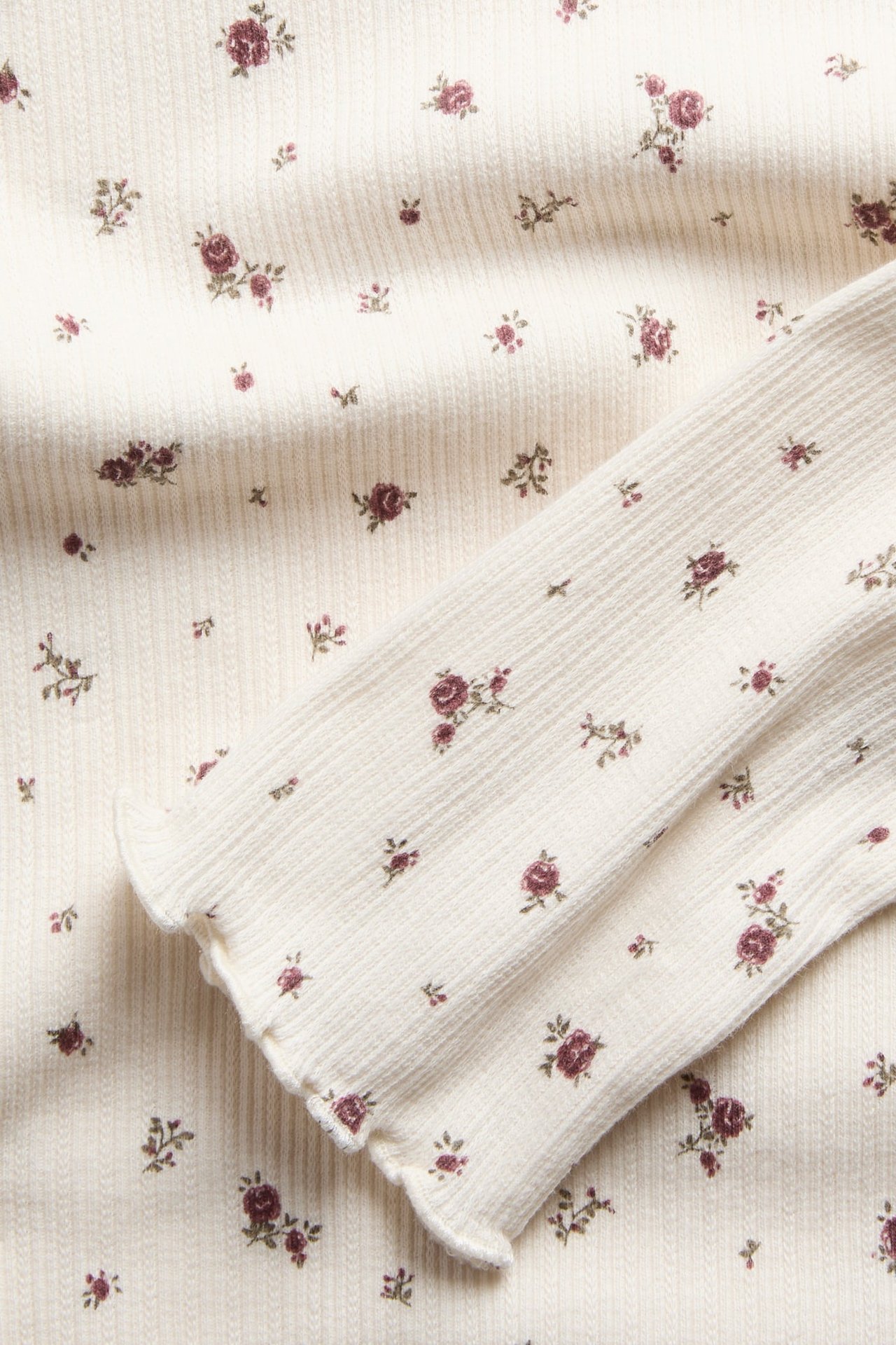 Close-up of a cream ribbed knit top with a dark red floral print and lettuce-edge cuff.