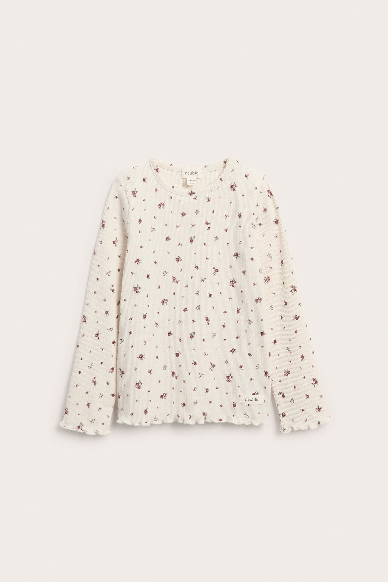Front view of a baby's off-white ribbed long-sleeve top with a red floral print and ruffled edges.