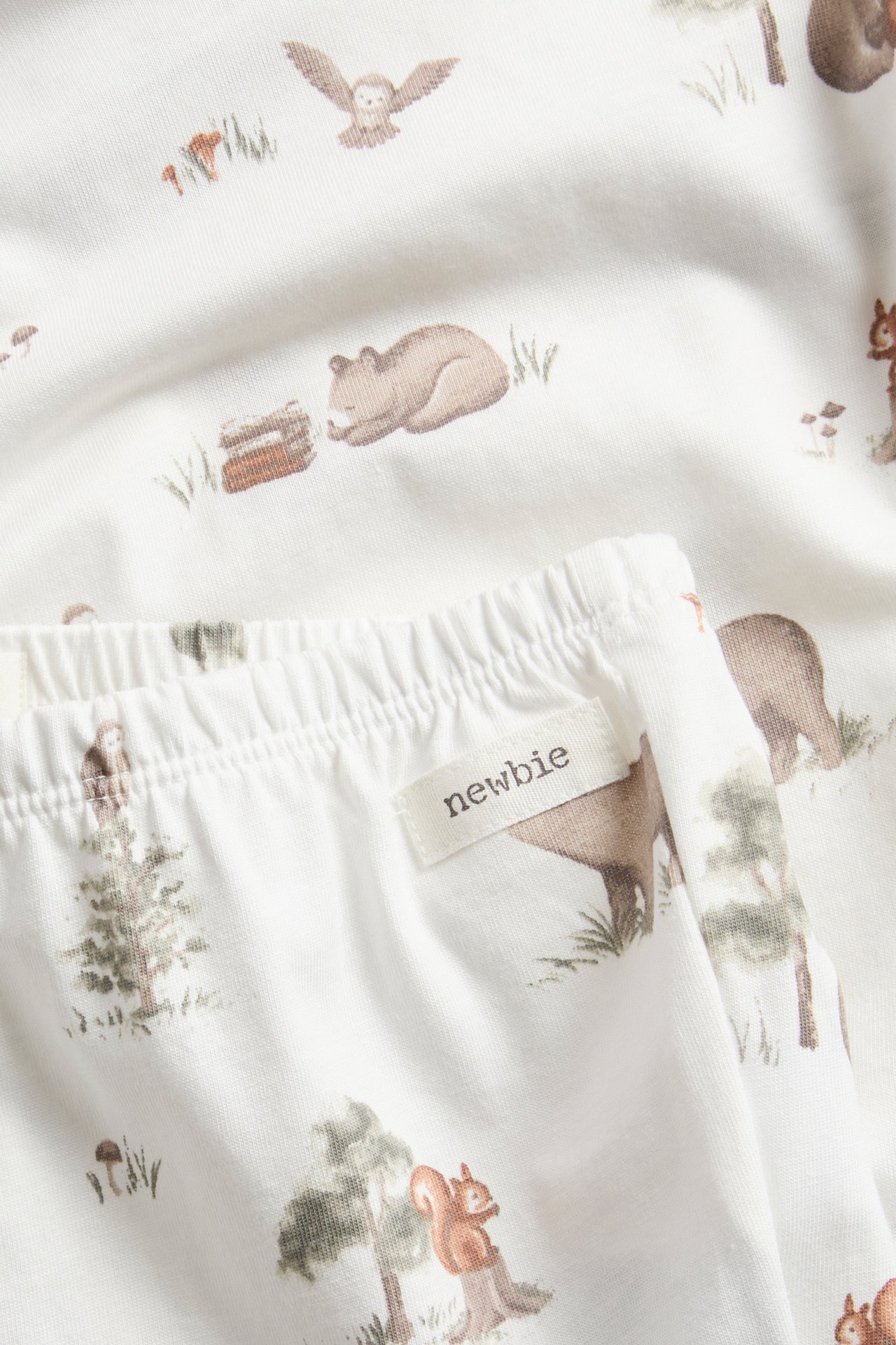 Nahaufnahme von weißen Babyhosen mit Gummibund und Waldtiermuster, mit passendem Oberteil.