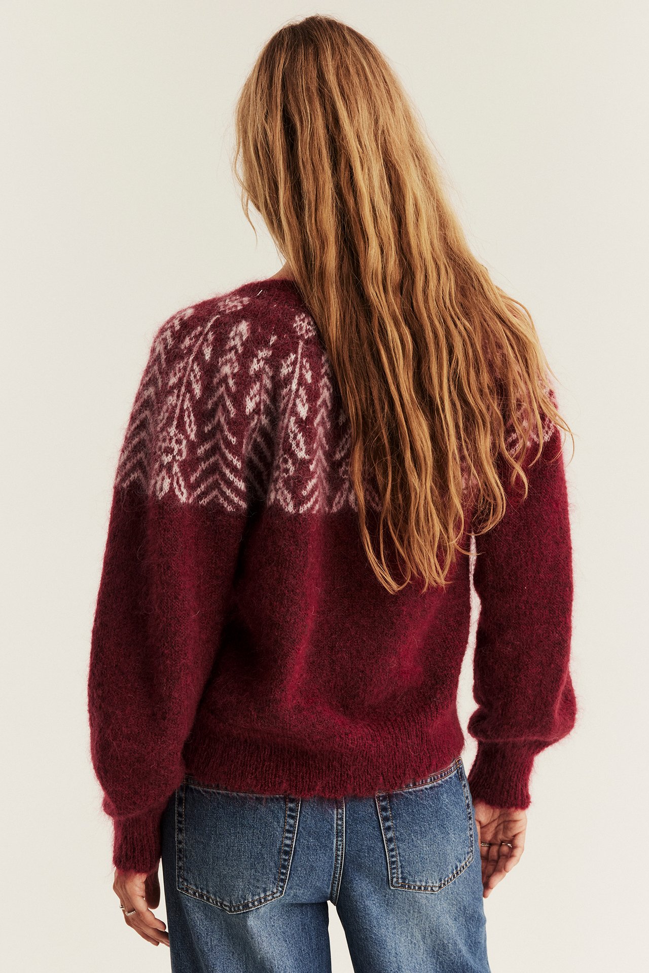 Rückansicht: Frau in dunkelrotem gemustertem Strickpullover und blauen Jeans.