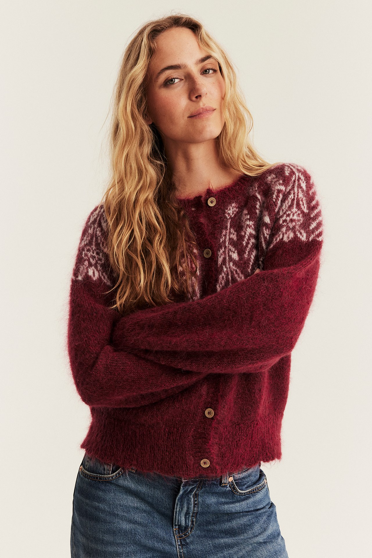Vorderansicht einer Frau in einem flauschigen bordeauxfarbenen Fair Isle Strickcardigan und Blue Jeans.