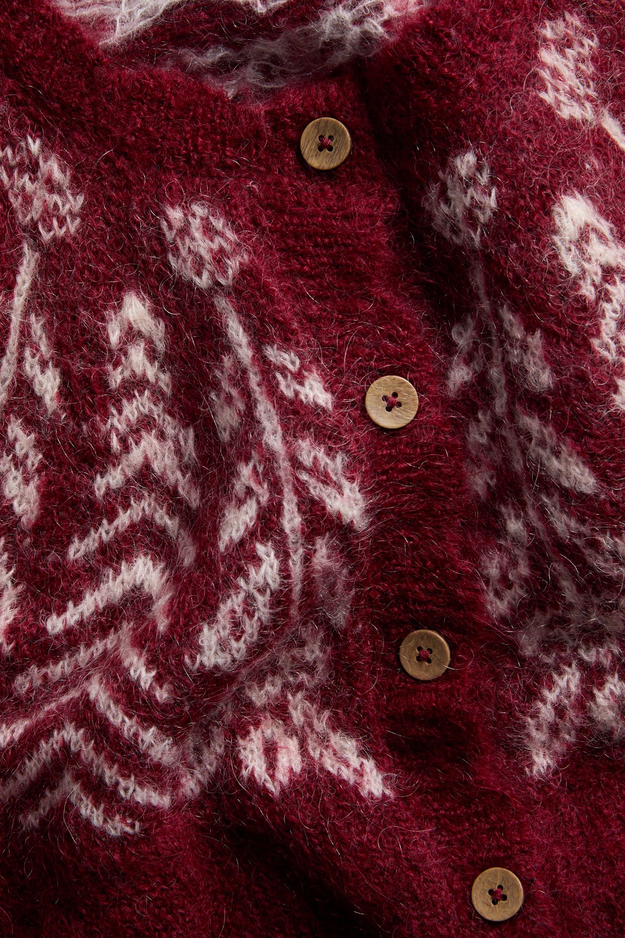 Nahaufnahme bordeauxrote Strickjacke mit weißem Fair Isle-Muster und Holzknöpfen.