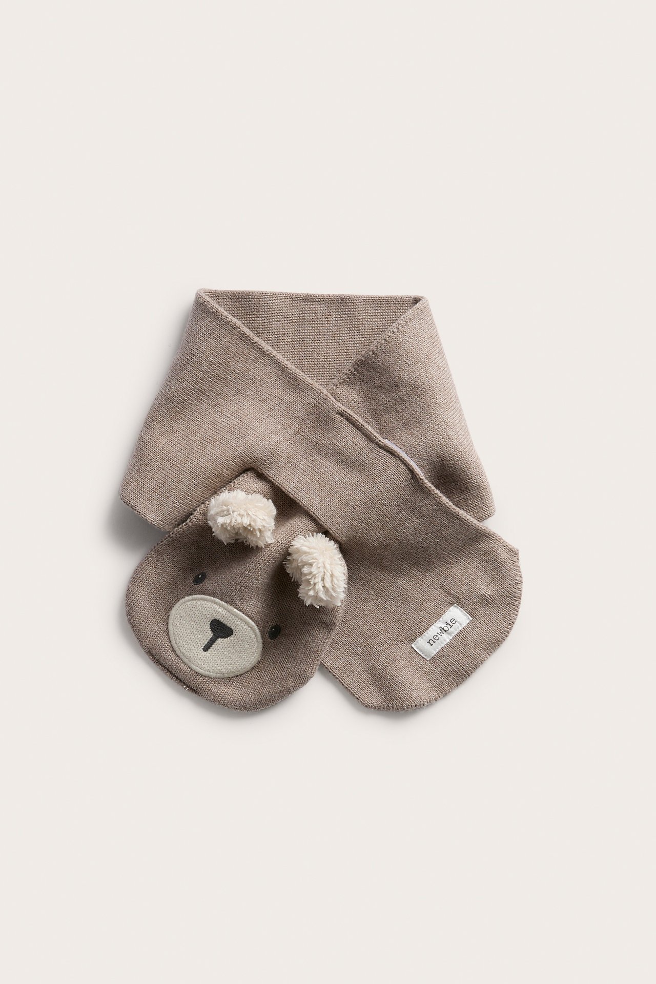 Gestrickter beiger Babyschal mit gesticktem Bärengesicht und zwei Pomponohren, Vorderansicht.