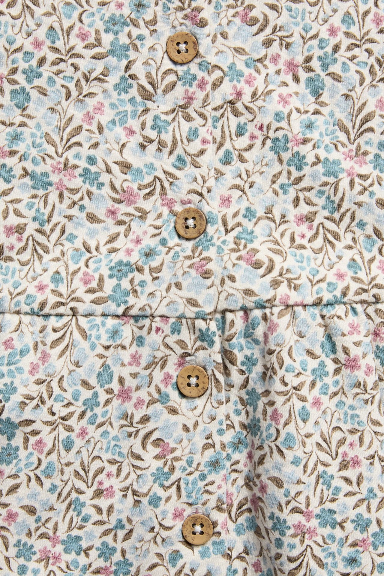 Close-up of cream floral fabric with blue, pink flowers, brown leaves, and wooden buttons.