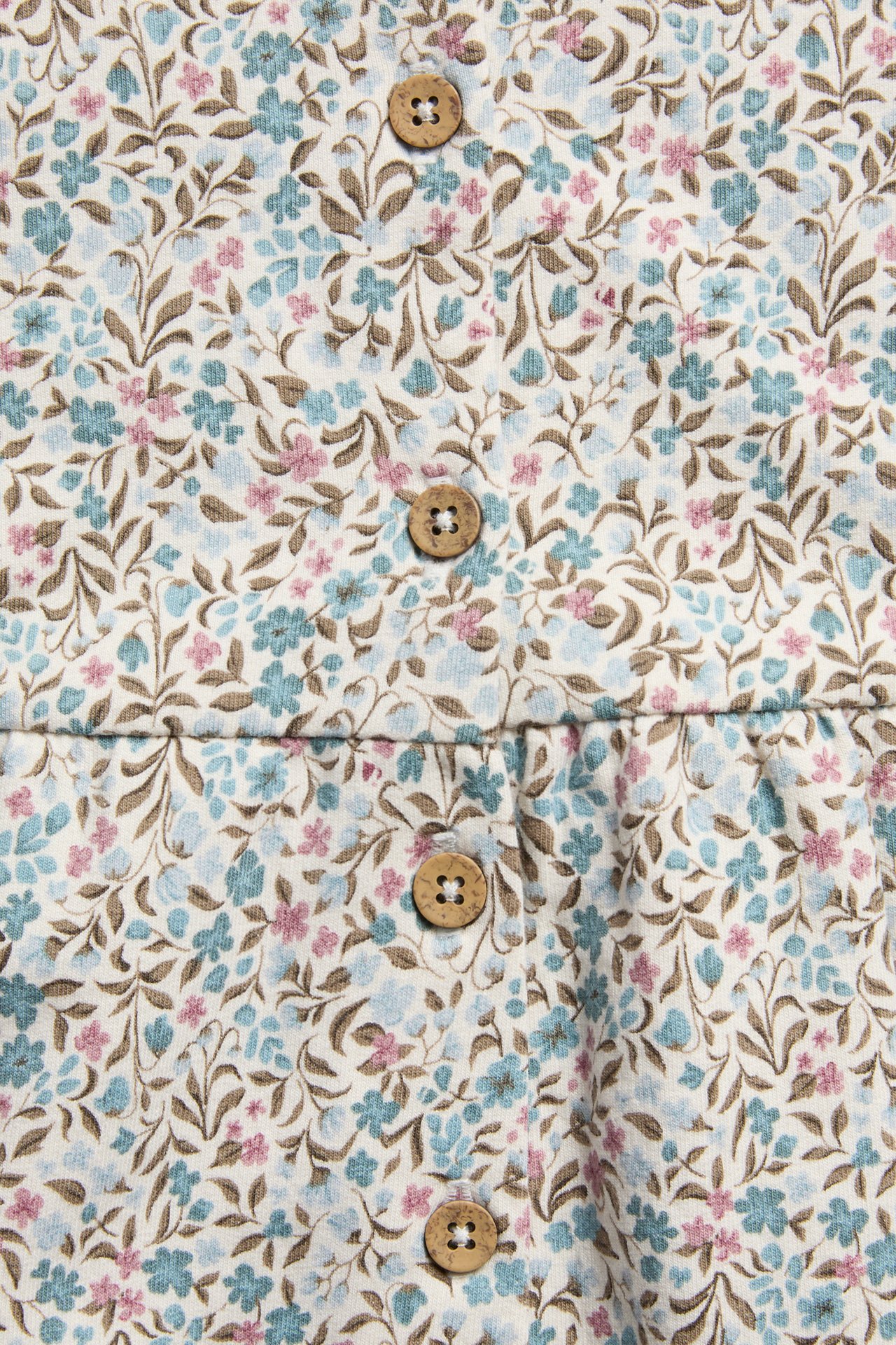 Nahaufnahme von cremefarbenem Blumenstoff mit blauen, rosa Blüten, braunen Blättern und Holzknöpfen.