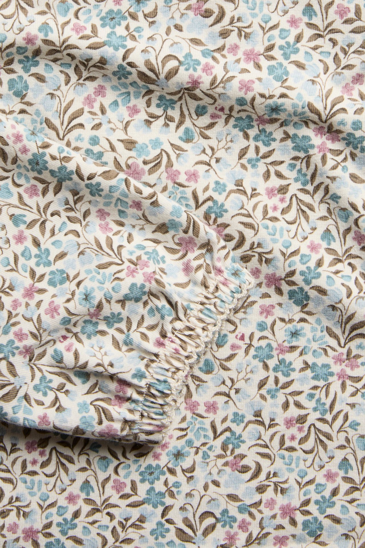 Nahaufnahme von cremefarbenem Cordstoff mit kleinem hellblauem, rosa und braunem Blumenmuster.