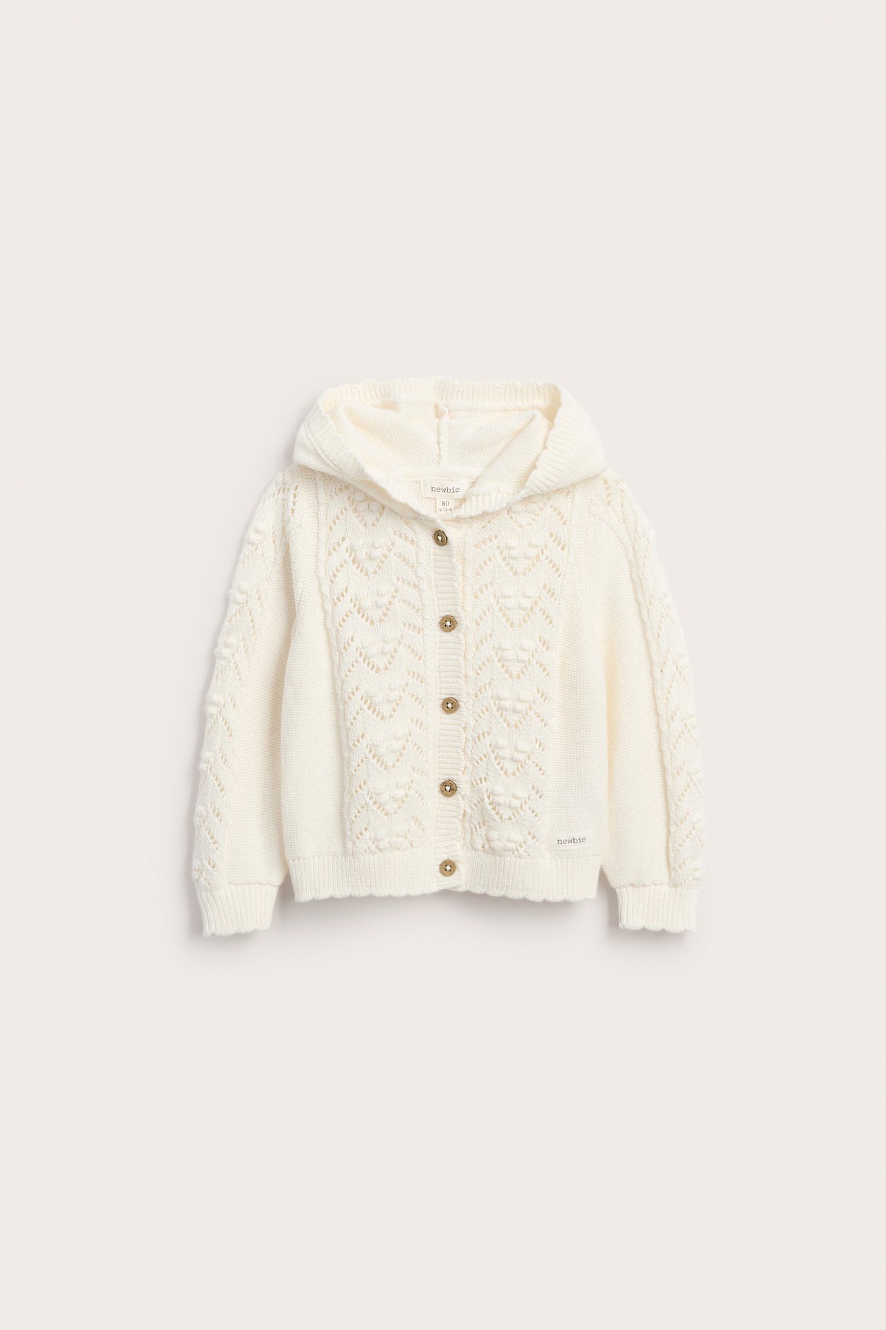 Vorderansicht einer cremeweißen Baby-Strickjacke mit Kapuze, Lochmuster und braunen Knöpfen.