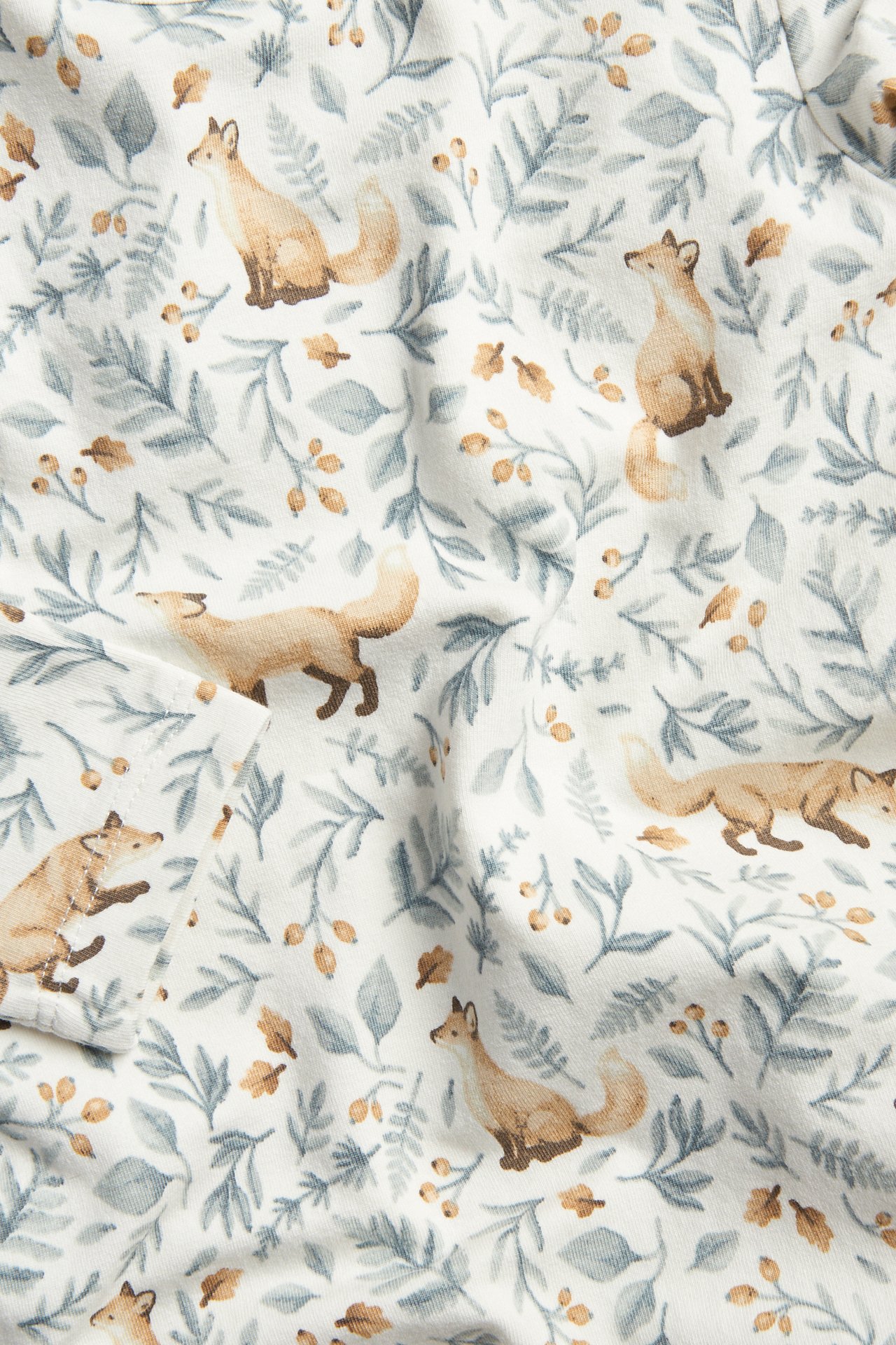 Close-up of white fabric with a watercolor-style pattern of brown foxes, blue leaves, and orange berries.