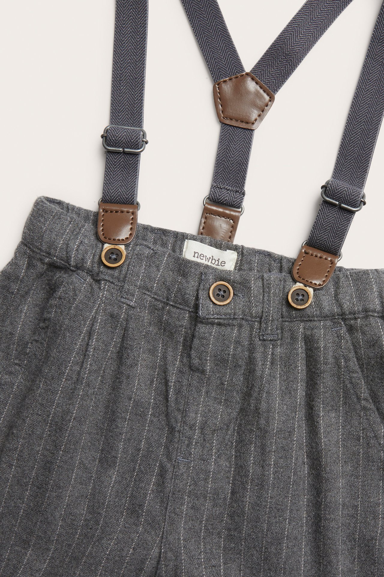 Close-up of grey pinstripe baby trousers with attached dark grey suspenders and brown leather details.