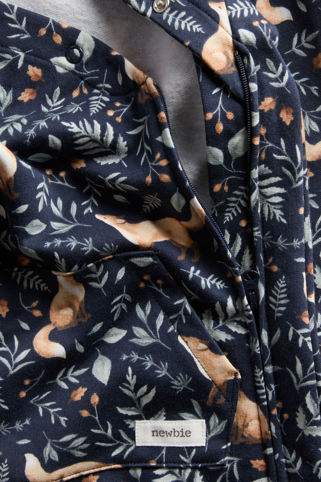 Close-up of a baby's dark blue fox and leaf print hooded overall with a front zipper.