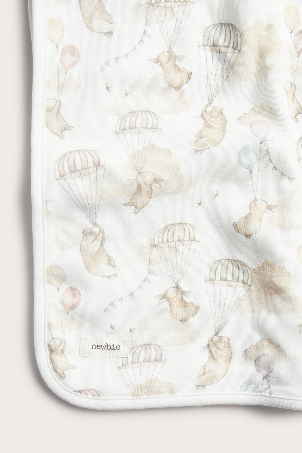 Close-up of an off-white cotton baby blanket with a pattern of bears, bunnies, parachutes, and balloons.