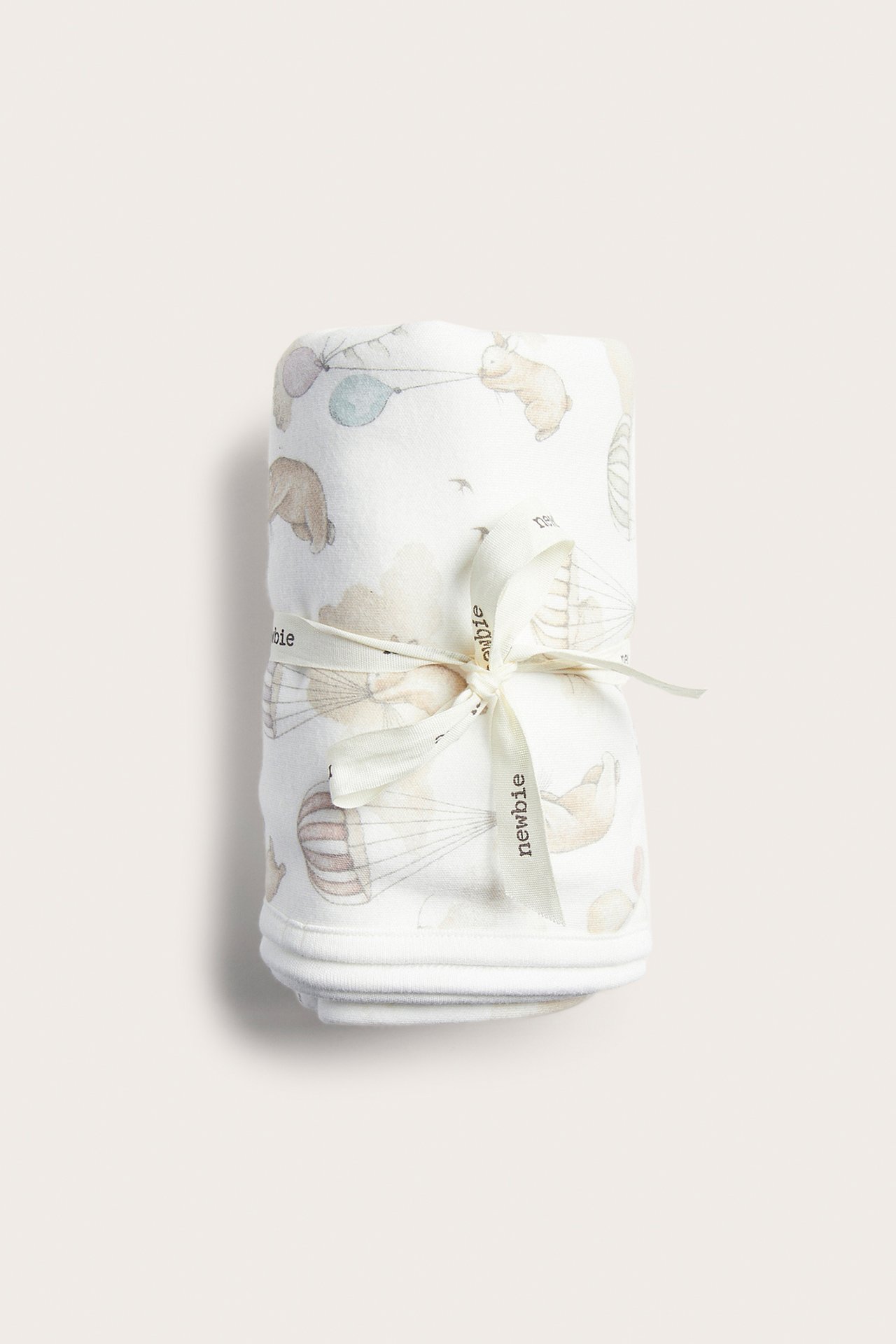 Rolled off-white cotton baby blanket with animal and hot air balloon pattern, tied with a ribbon.