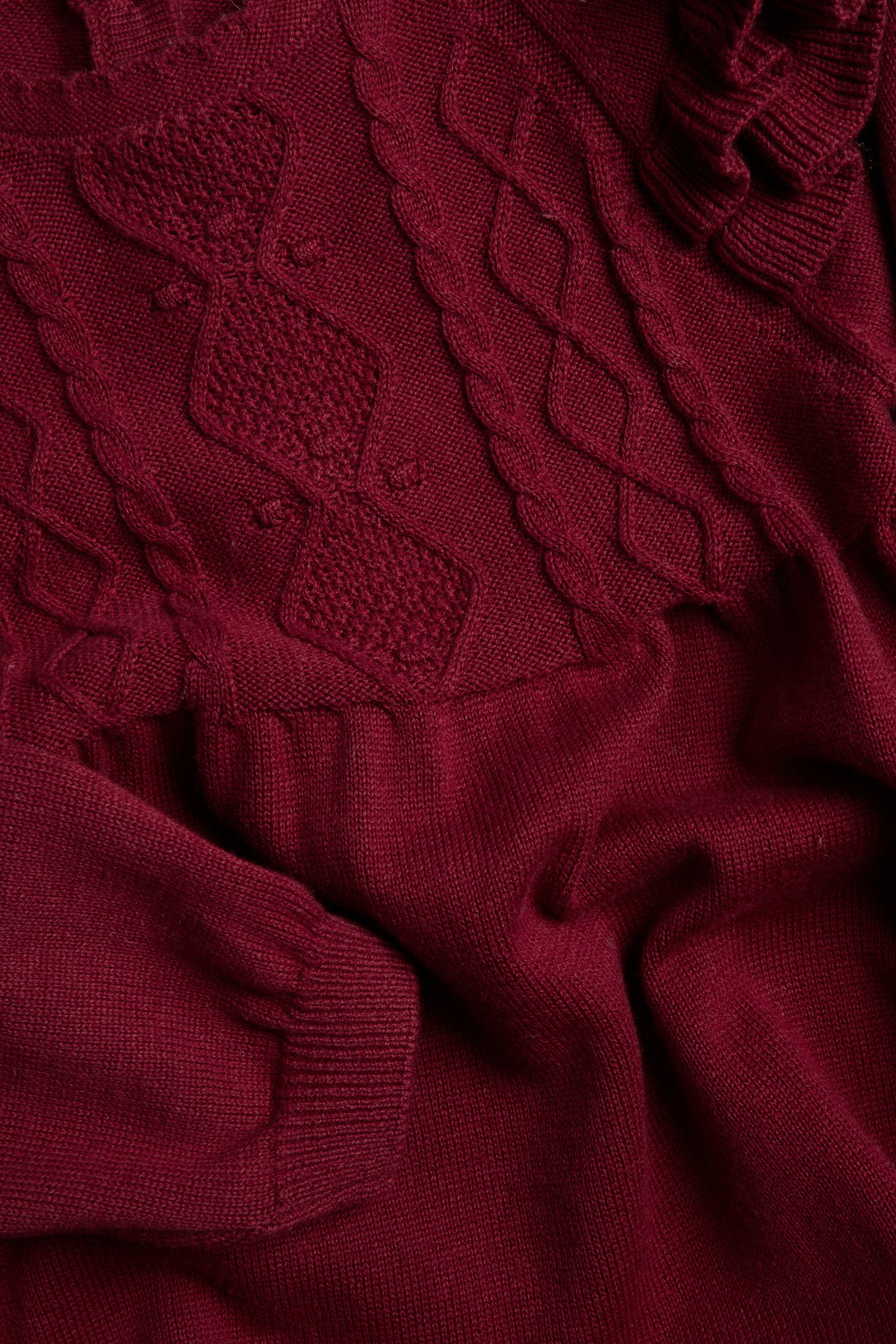 Nahaufnahme eines weinroten Strickpullovers mit Zopf- und Rautenmuster.