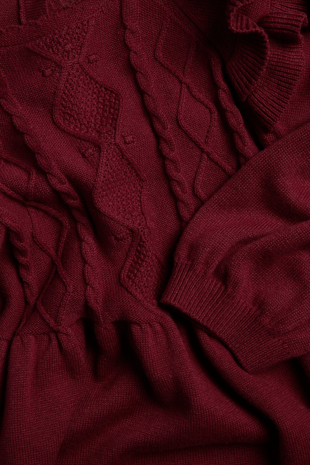 Close-up of a burgundy knitted sweater with cable knit patterns and ribbed cuffs.