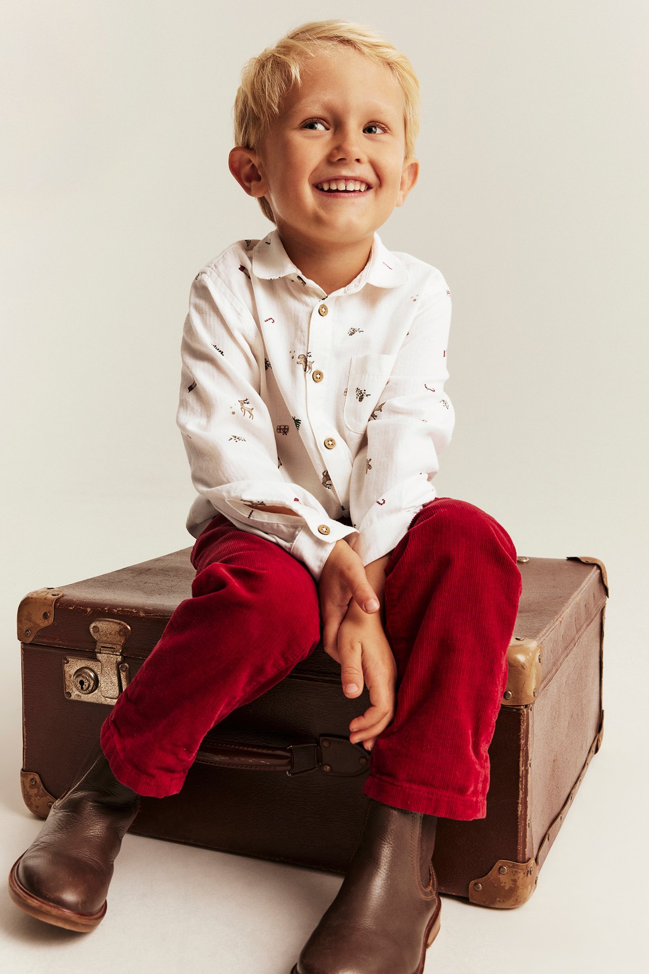 Front view: kid wears white printed shirt, red corduroy pants, and brown boots.