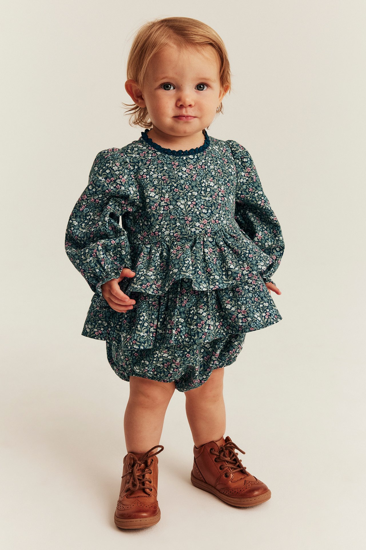 Front view: Baby in dark green floral ruffled top and matching bloomers with brown lace-up shoes.