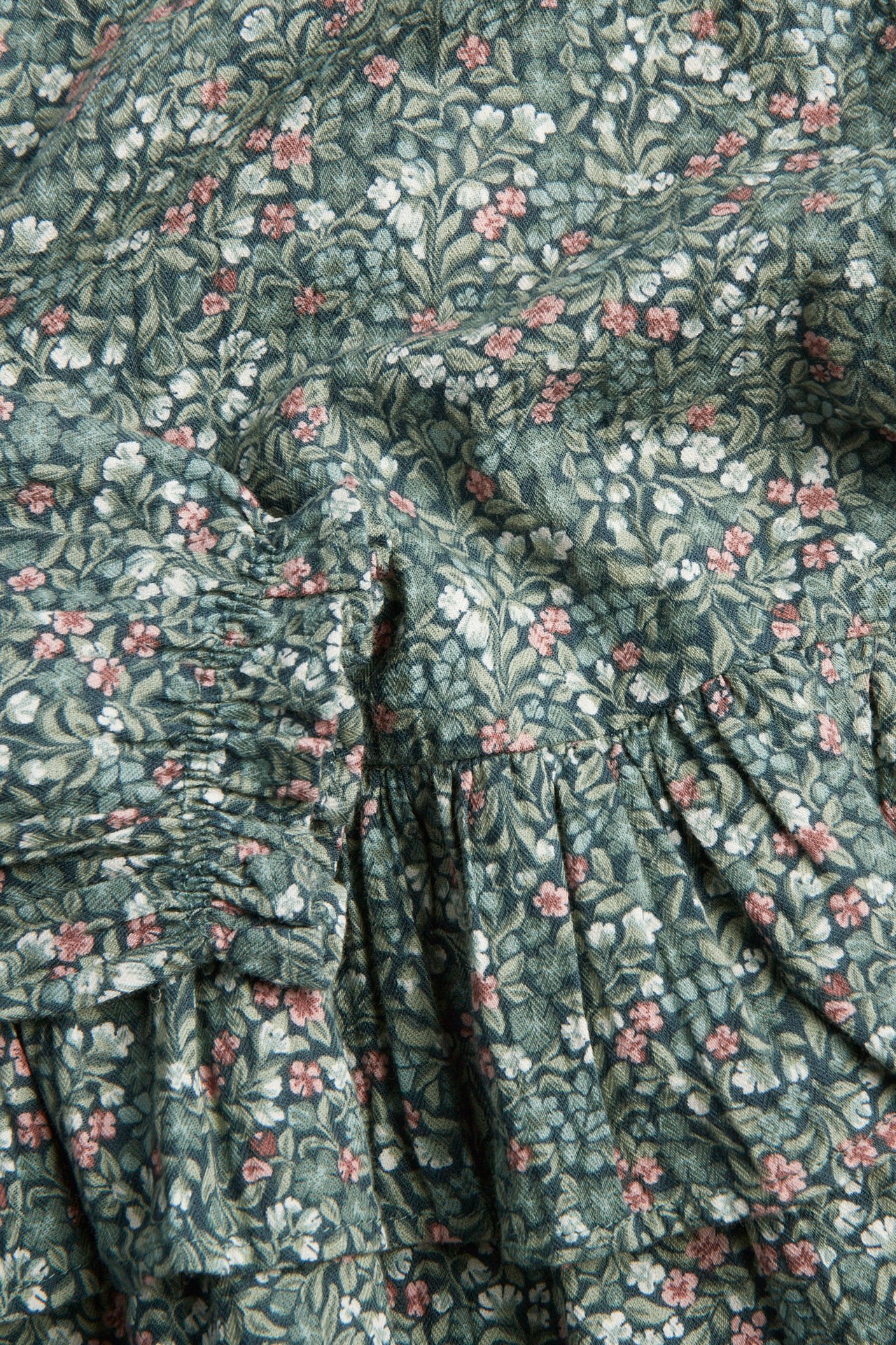 Nahaufnahme von dunkelgrünem Stoff mit weißem und rosa Blumenmuster und gerafften Details.