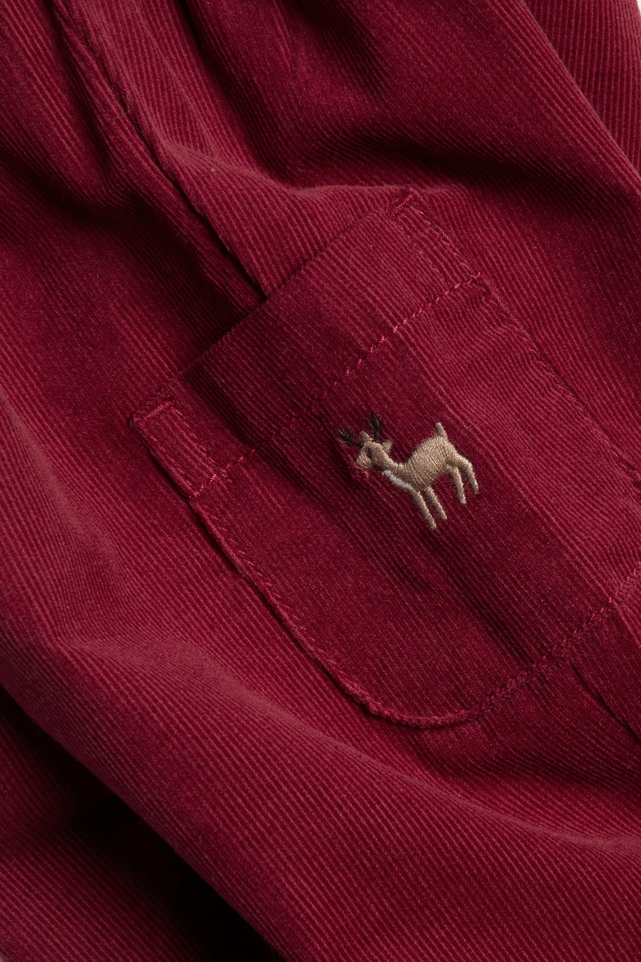 Close-up of burgundy corduroy garment with an embroidered deer on a pocket.