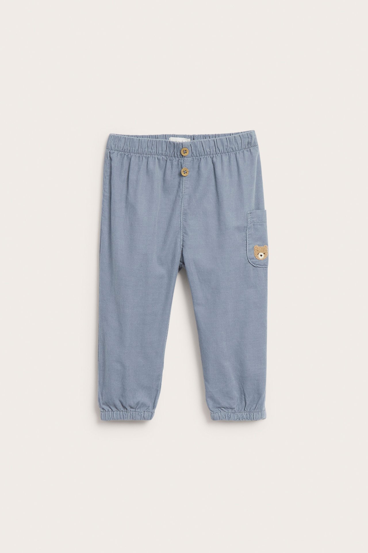 Vorderansicht blauer Babyhose mit Gummibund, zwei Knöpfen und gesticktem Teddybär auf Tasche.