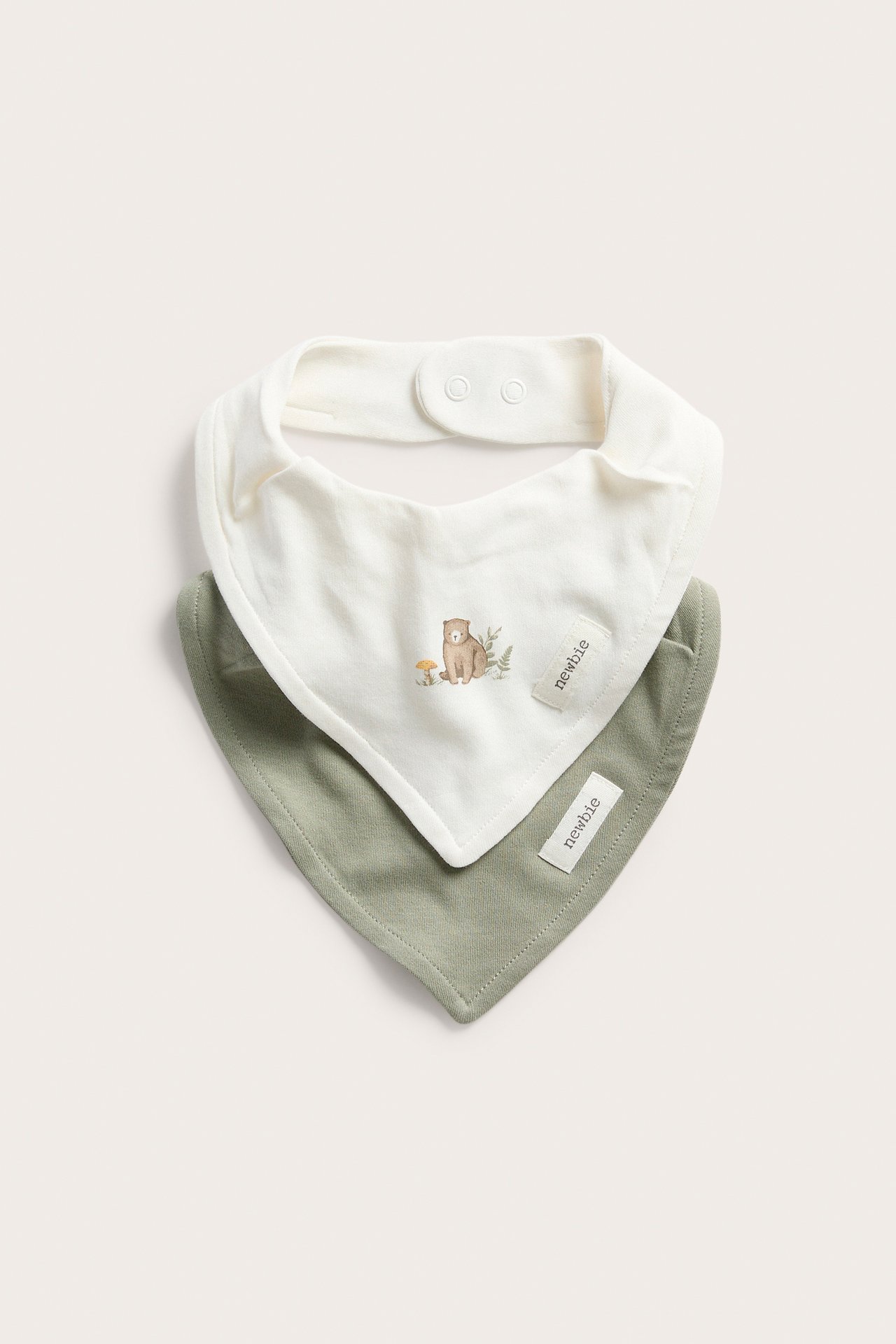 Front view of two baby bibs: one off-white with a bear pattern, one plain light green, with snap buttons.