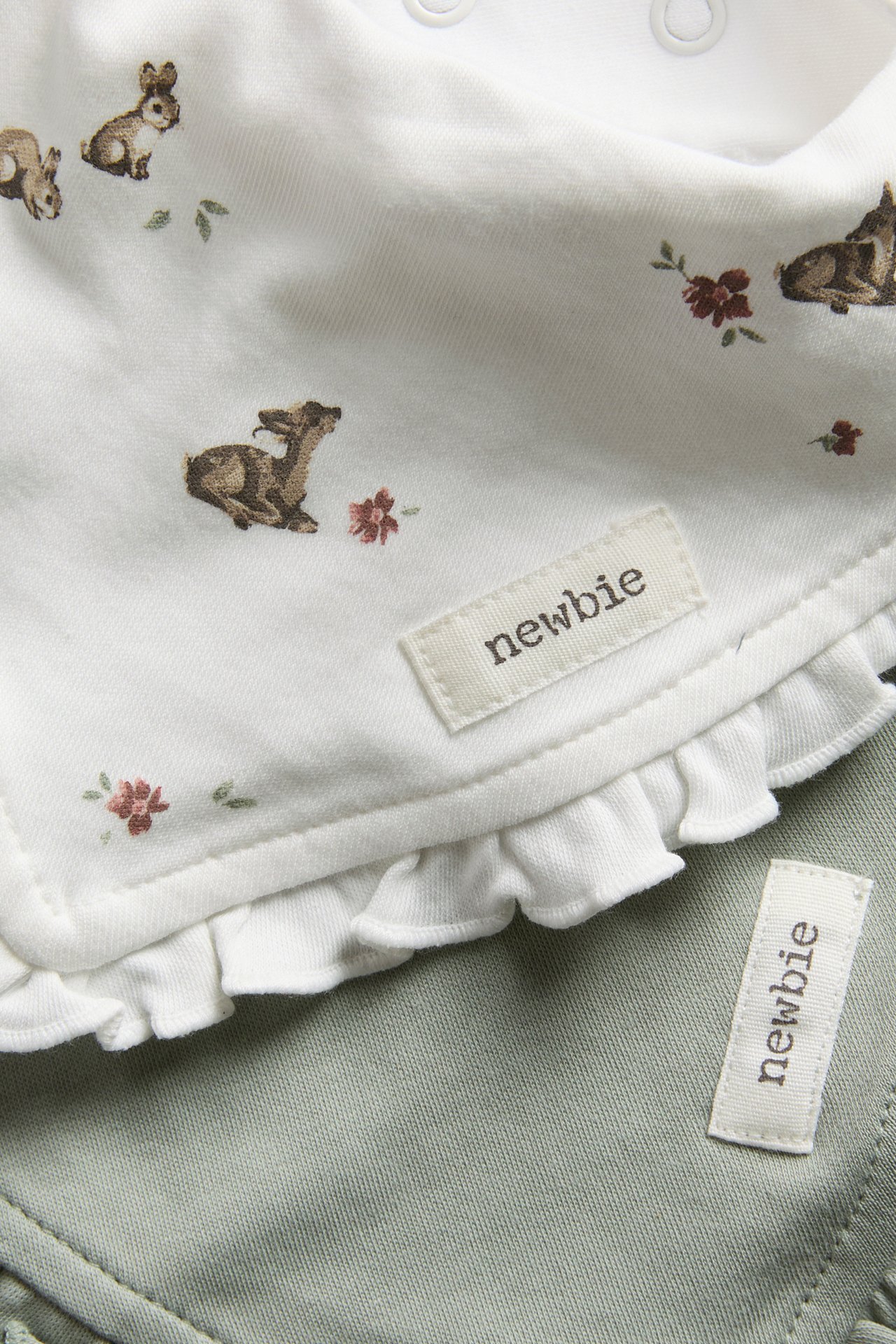 Close-up of a white baby bib with animal print and ruffled edge, over a sage green garment.