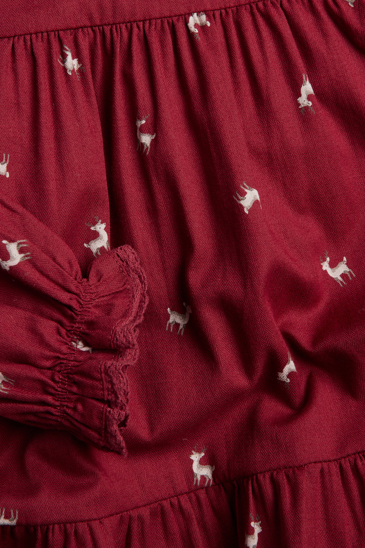 Close-up of a dark red herringbone fabric with white deer print and gathered sleeve cuff.