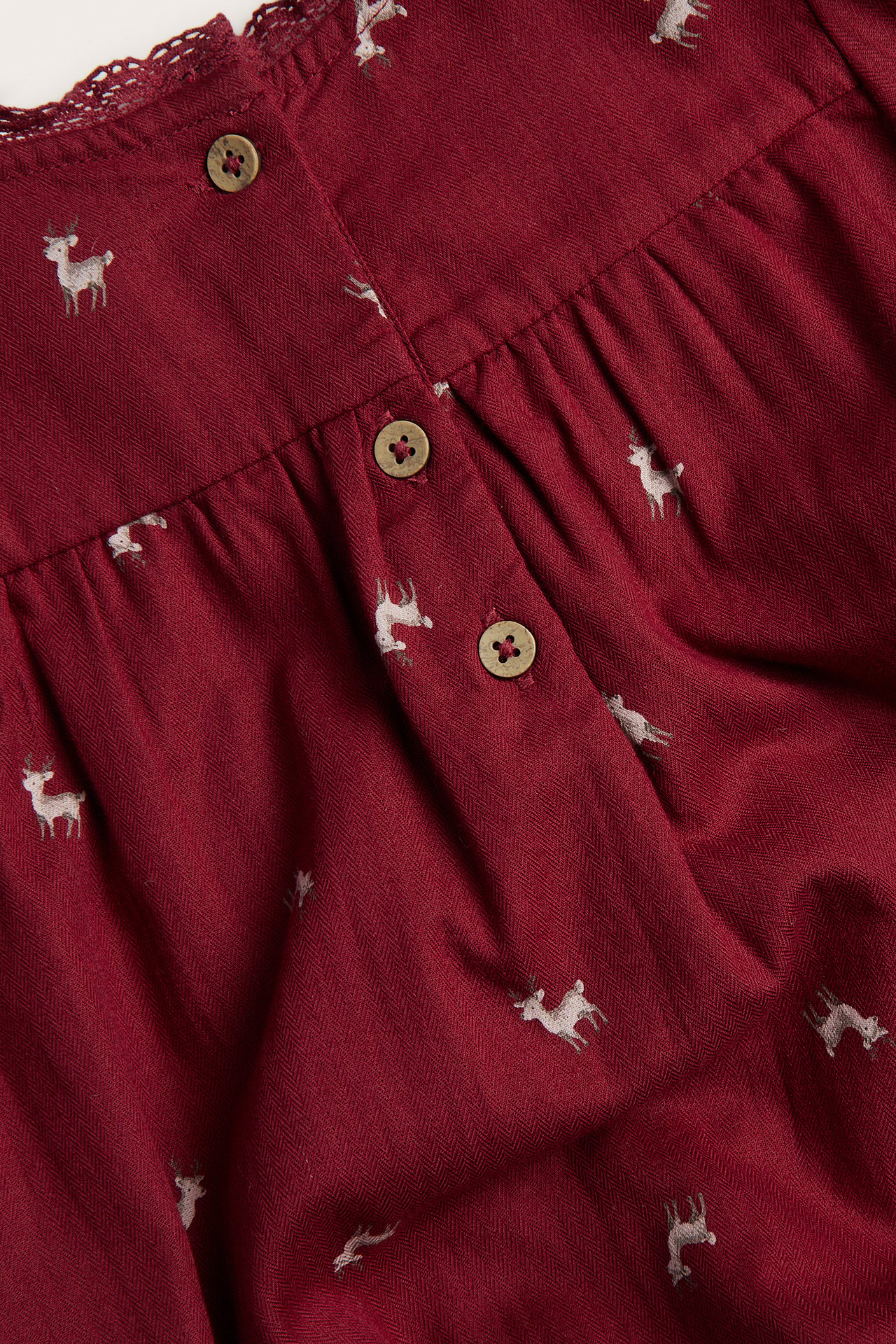 Close-up of a maroon dress with a herringbone pattern, white deer print, and three wooden buttons.