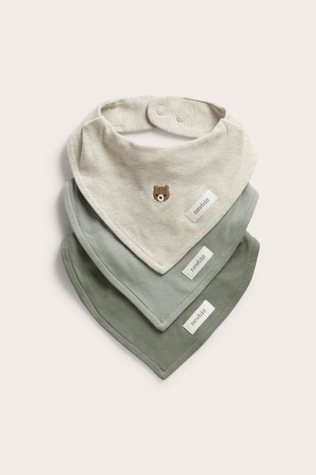Stacked front view of three baby bandana bibs: light beige with bear embroidery, light sage, and olive green.