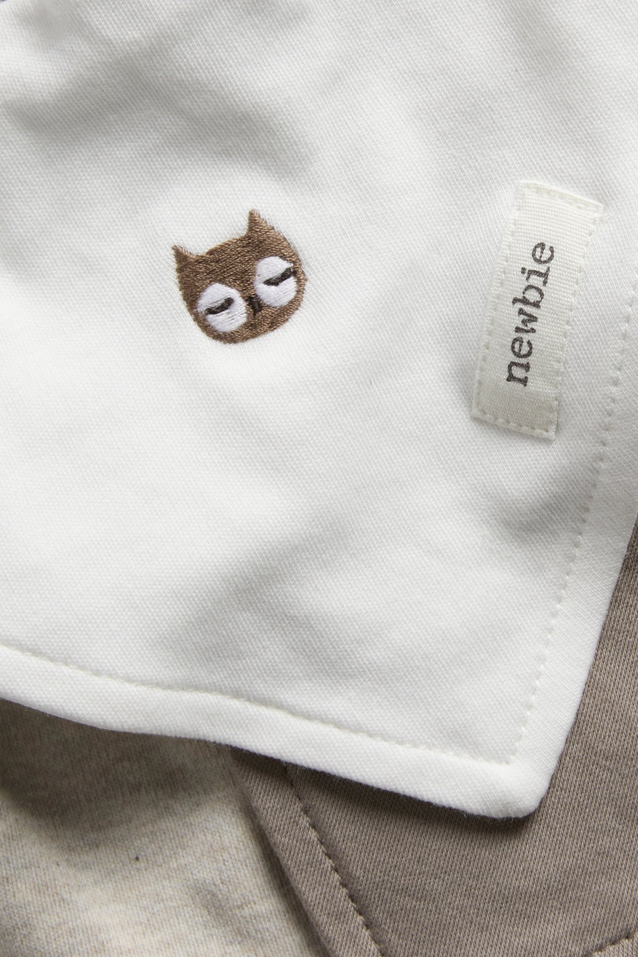 Close-up of a white baby textile with a brown embroidered owl and a 'newbie' tag.