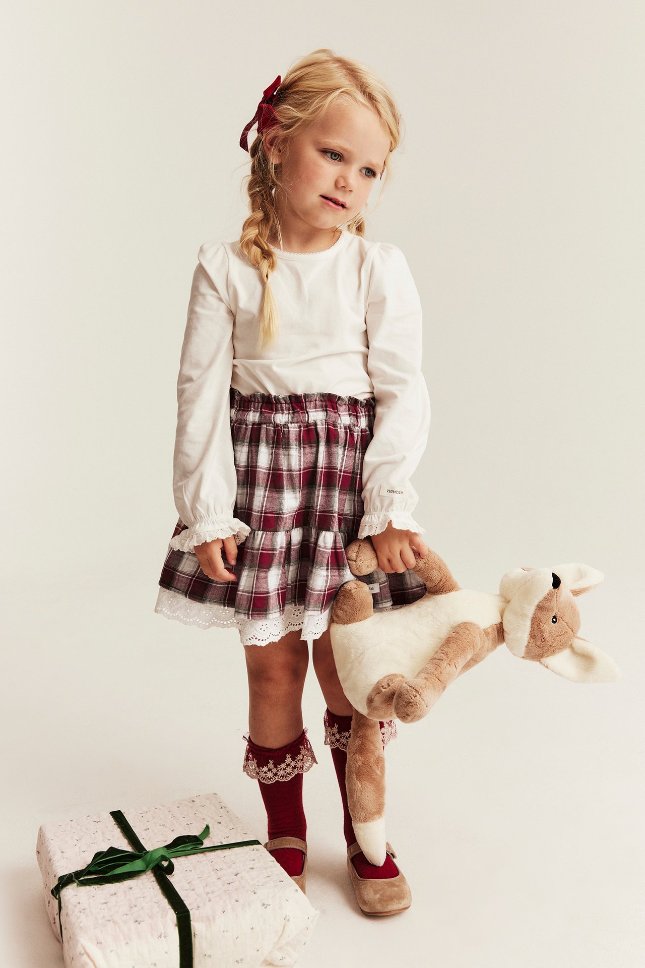 Front view: Kid in white ruffled shirt, red plaid tiered skirt, red lace-trim socks, and tan shoes.